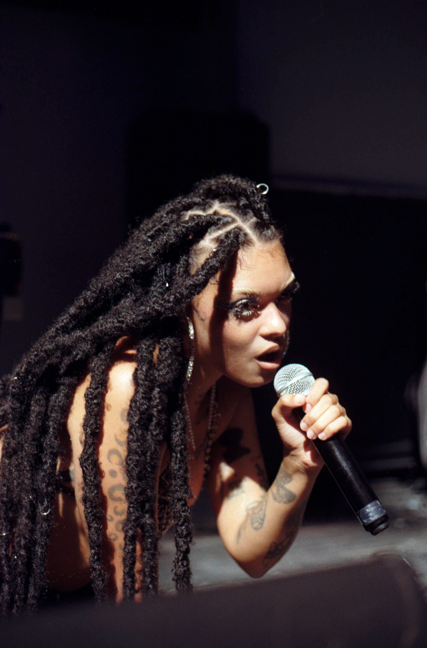 Close-up of tattooed female singer with locs performing with handheld microphone on stage.
