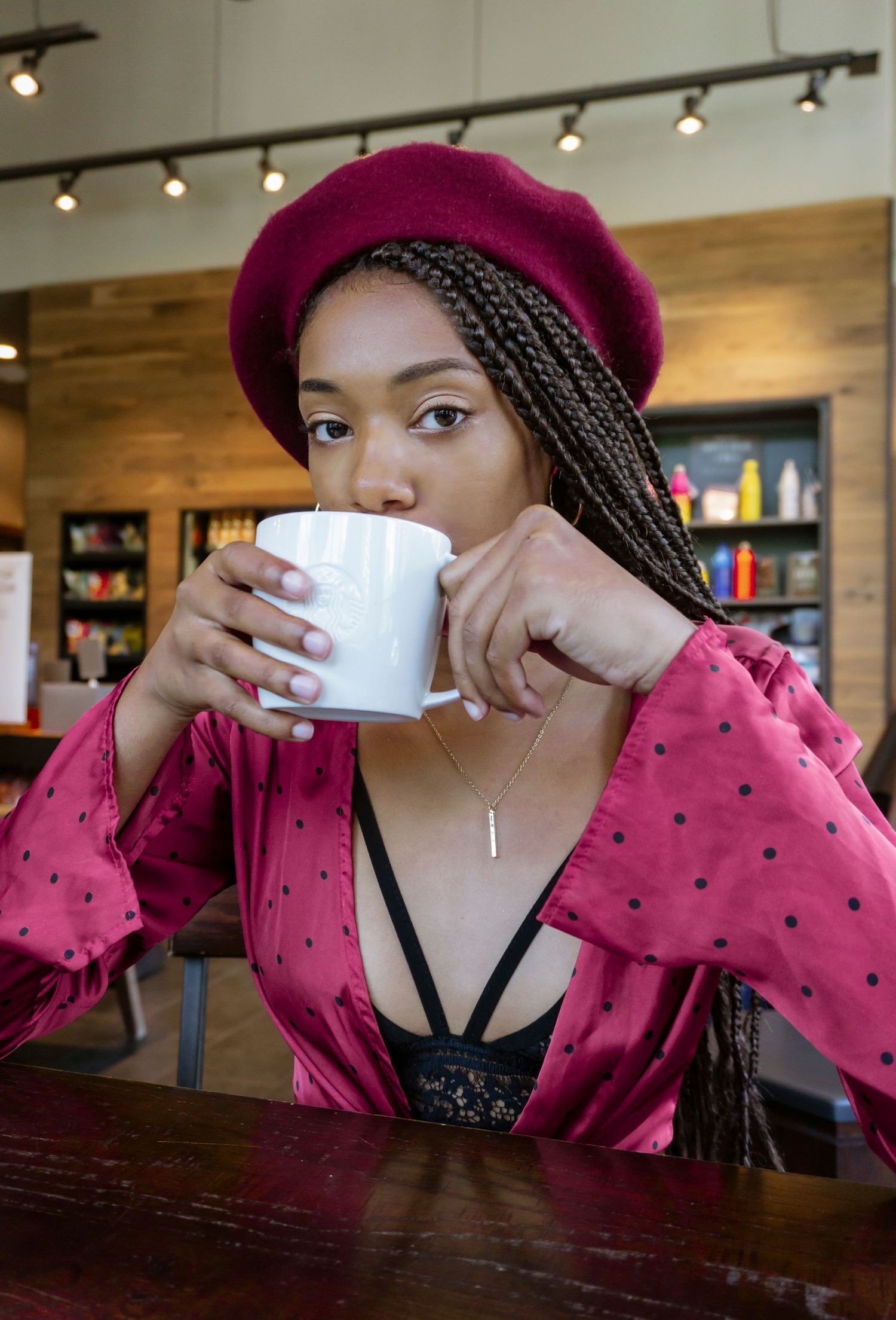 Stylish woman in red beret and pink robe drinking coffee at a cafe table.