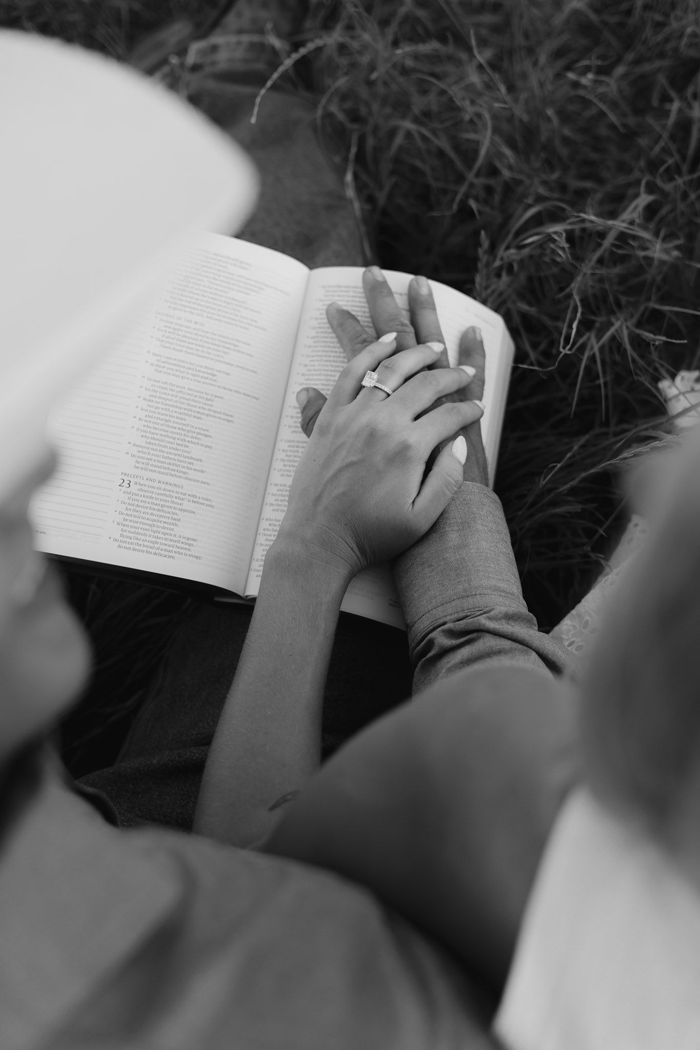 Couple holding hands over an open Bible in a black and white romantic outdoor engagement photo.