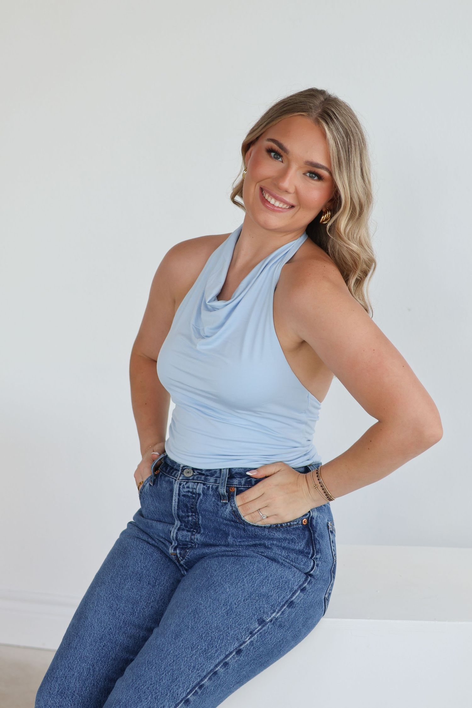 A person in a light blue tank top and high-waisted jeans poses against a white backdrop from different angles.