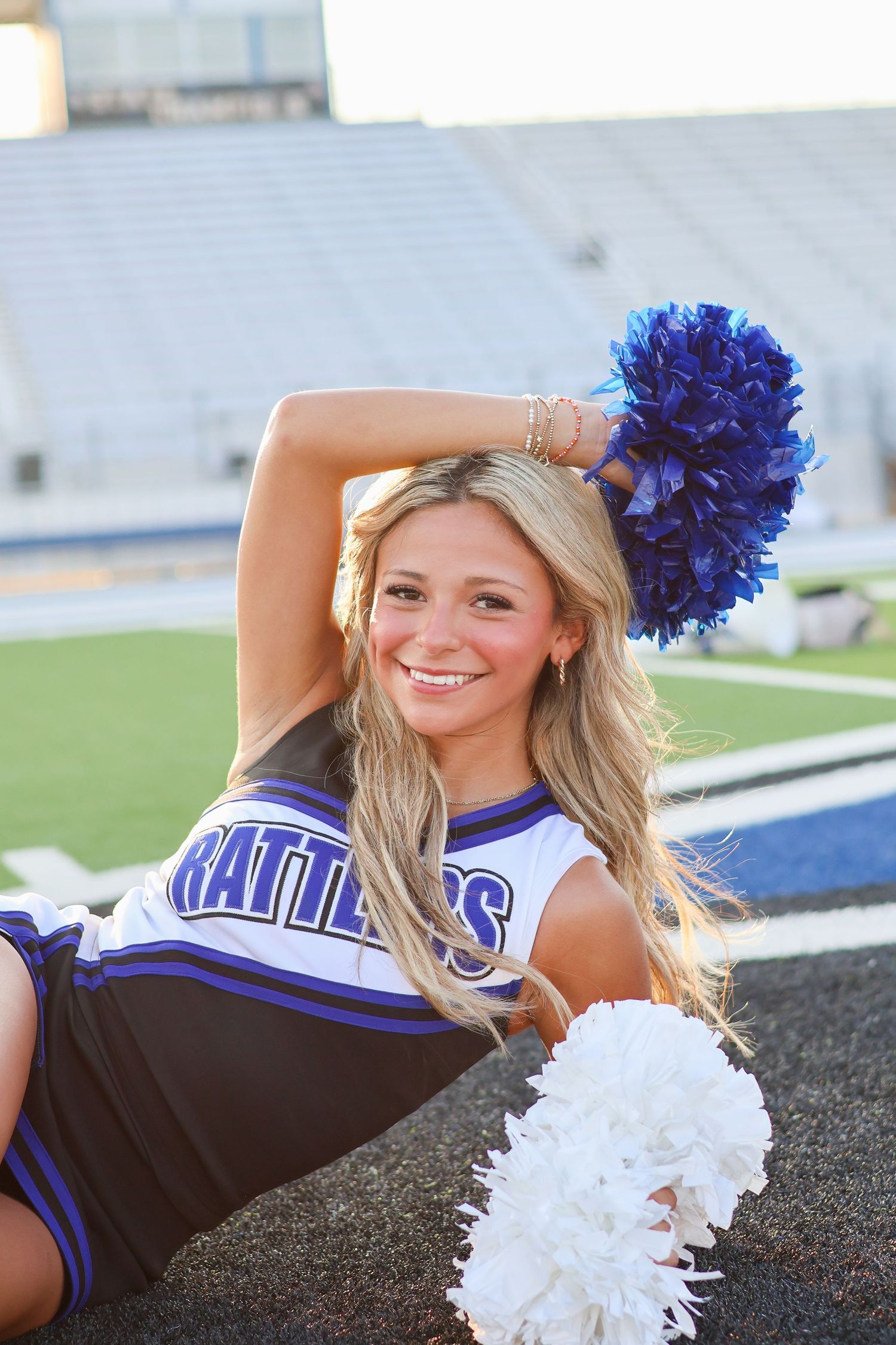 Cheerleader with blue and white pom poms poses on field.
