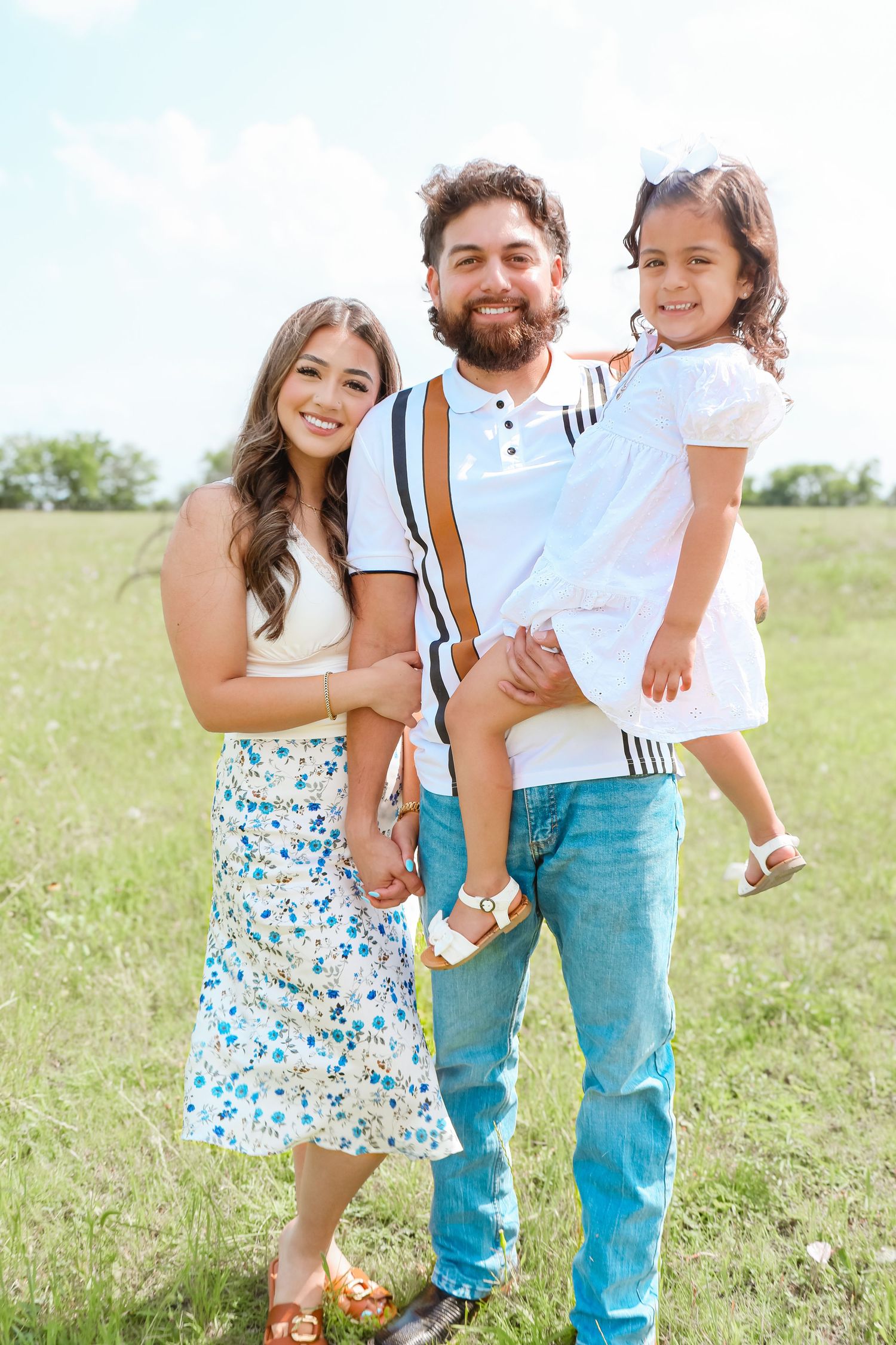 Family in coordinated outfits laughing together in sunny meadow during spring photo session.