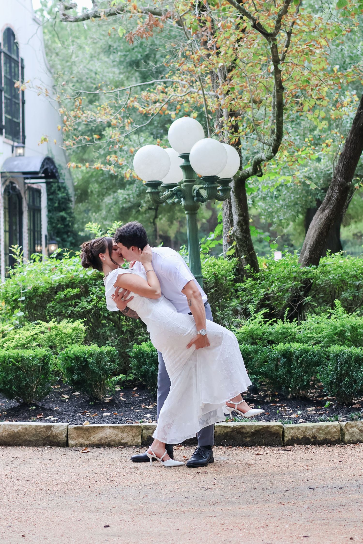 A romantic dance dip pose captured in a park setting with trees and greenery in the background.