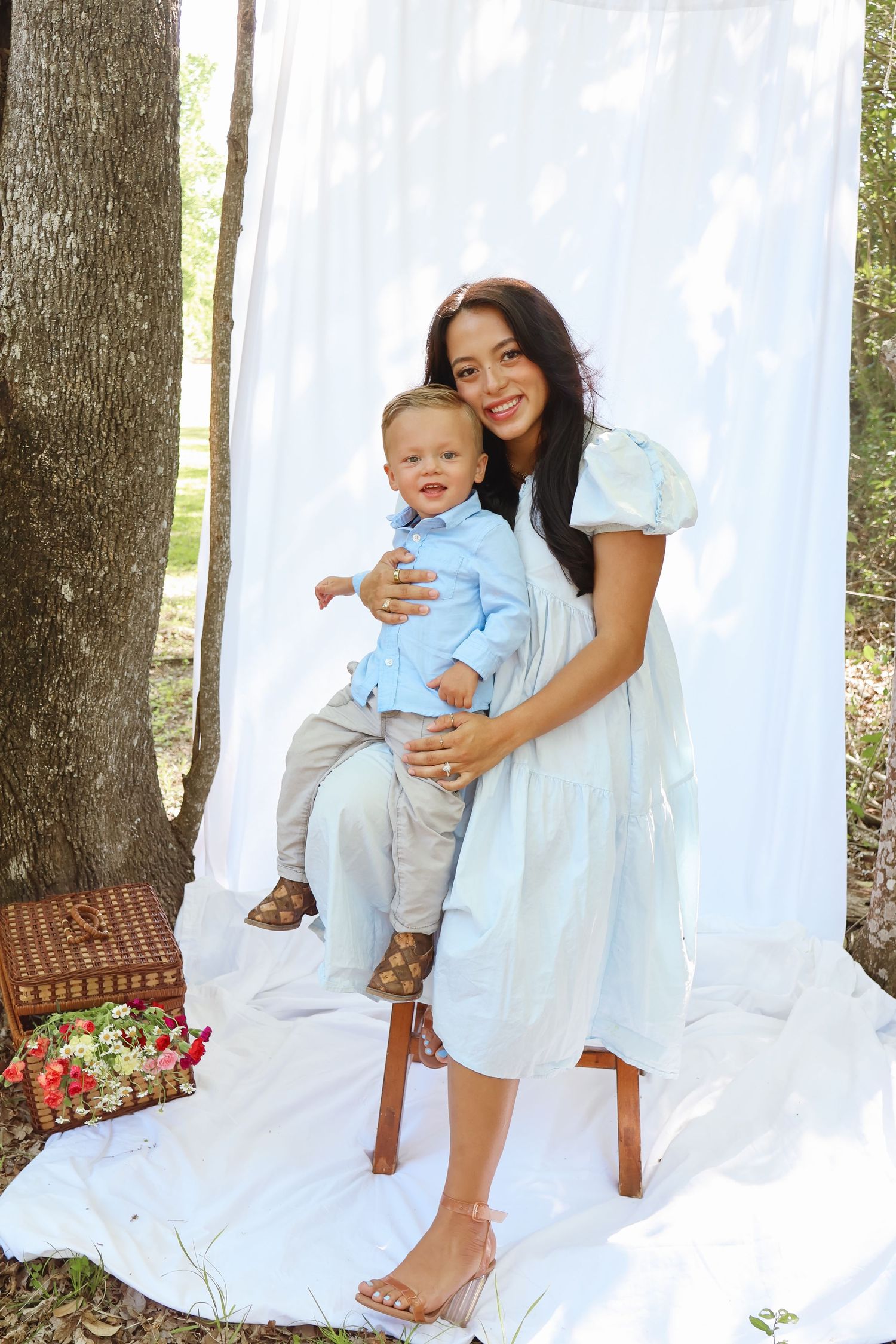 Mother and baby in light blue outfits posing against white backdrop for outdoor photo session.