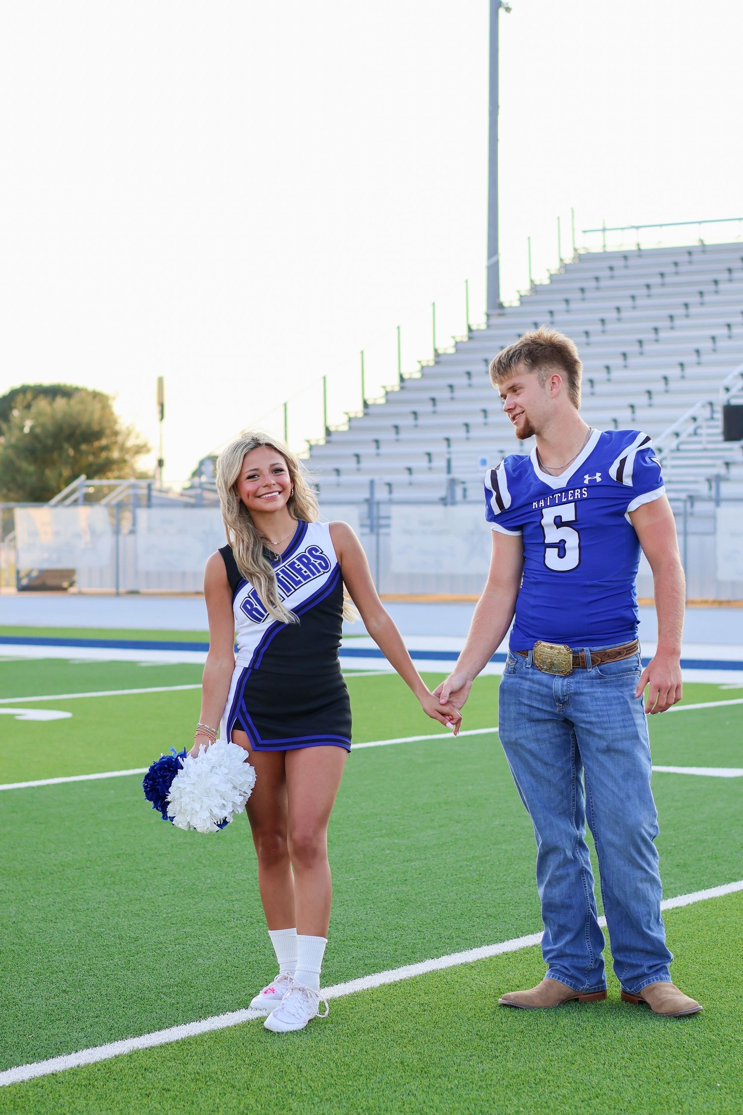 Cheerleader and football player holding hands on football field.