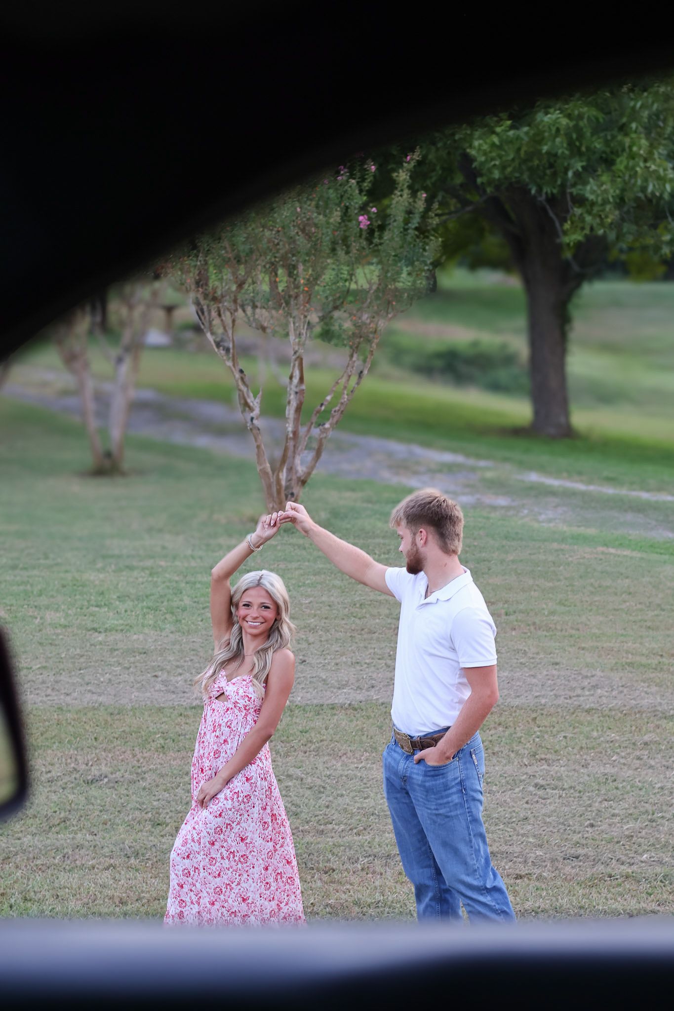 A couple dancing together in a grassy outdoor setting, with the person in a floral dress twirling gracefully.