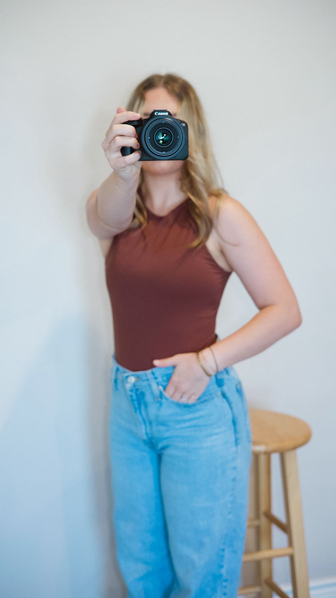 Person in maroon top and blue jeans holding a camera against white background.