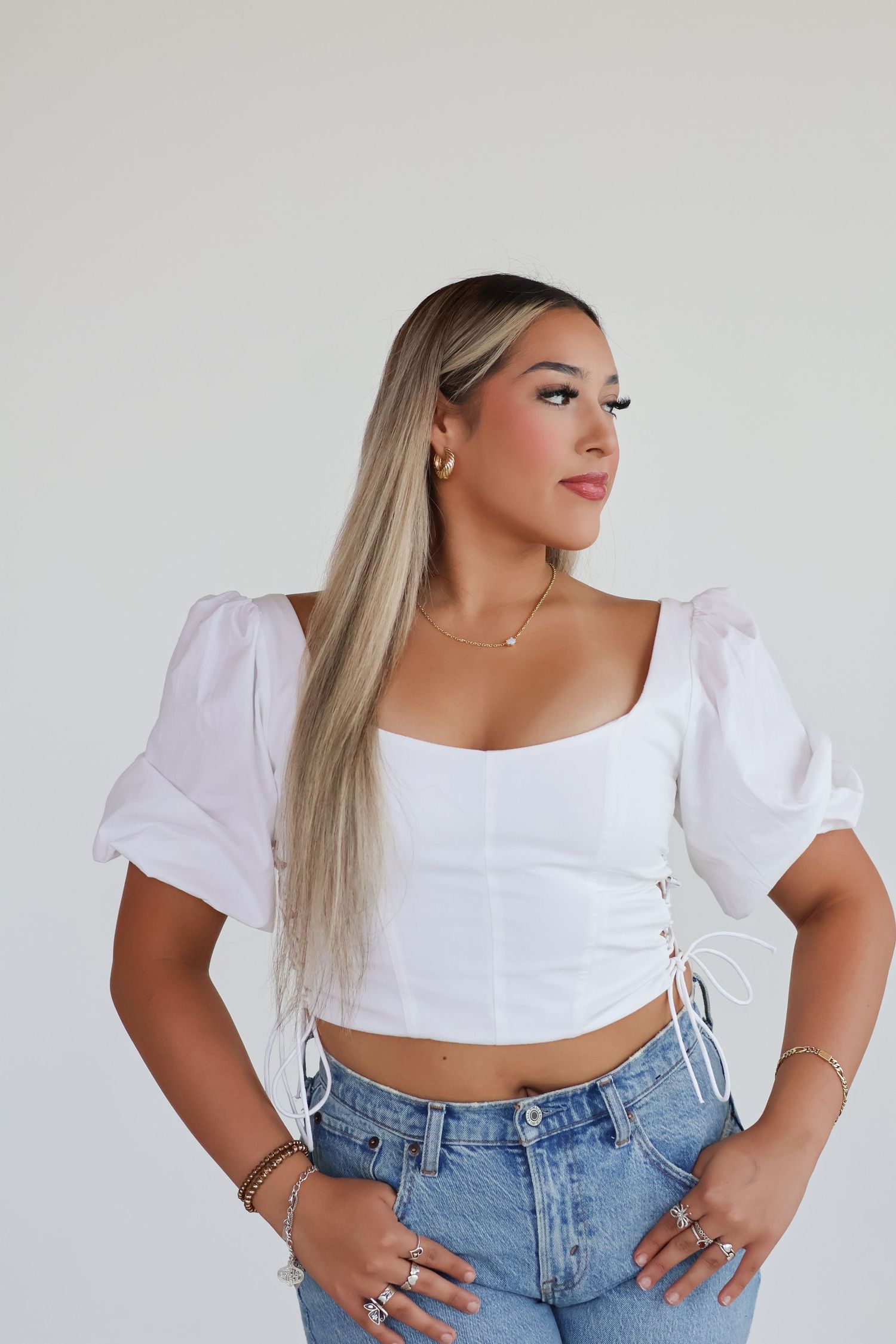 A person wearing a white cropped top with puff sleeves and high-waisted blue jeans poses against a white background.