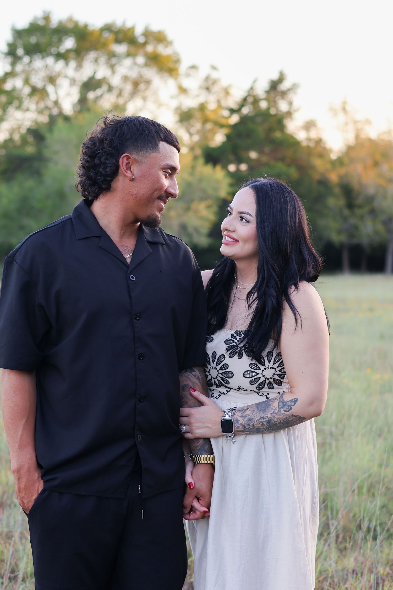 A couple shares intimate moments in a grassy field at sunset wearing contrasting black and white outfits.