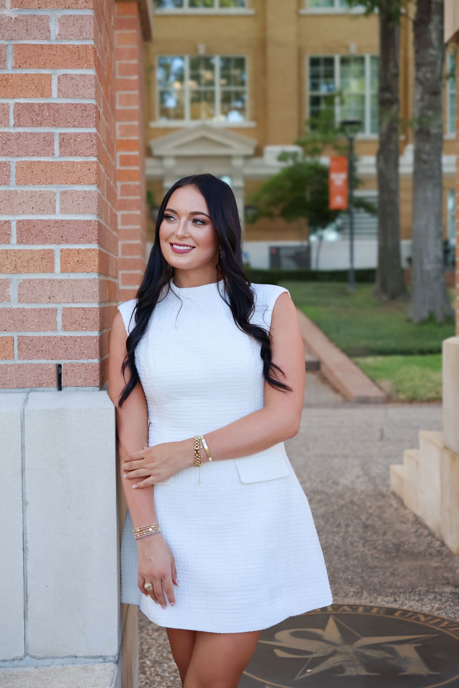 Professional graduation portrait session featuring a white sleeveless dress against a brick building backdrop.