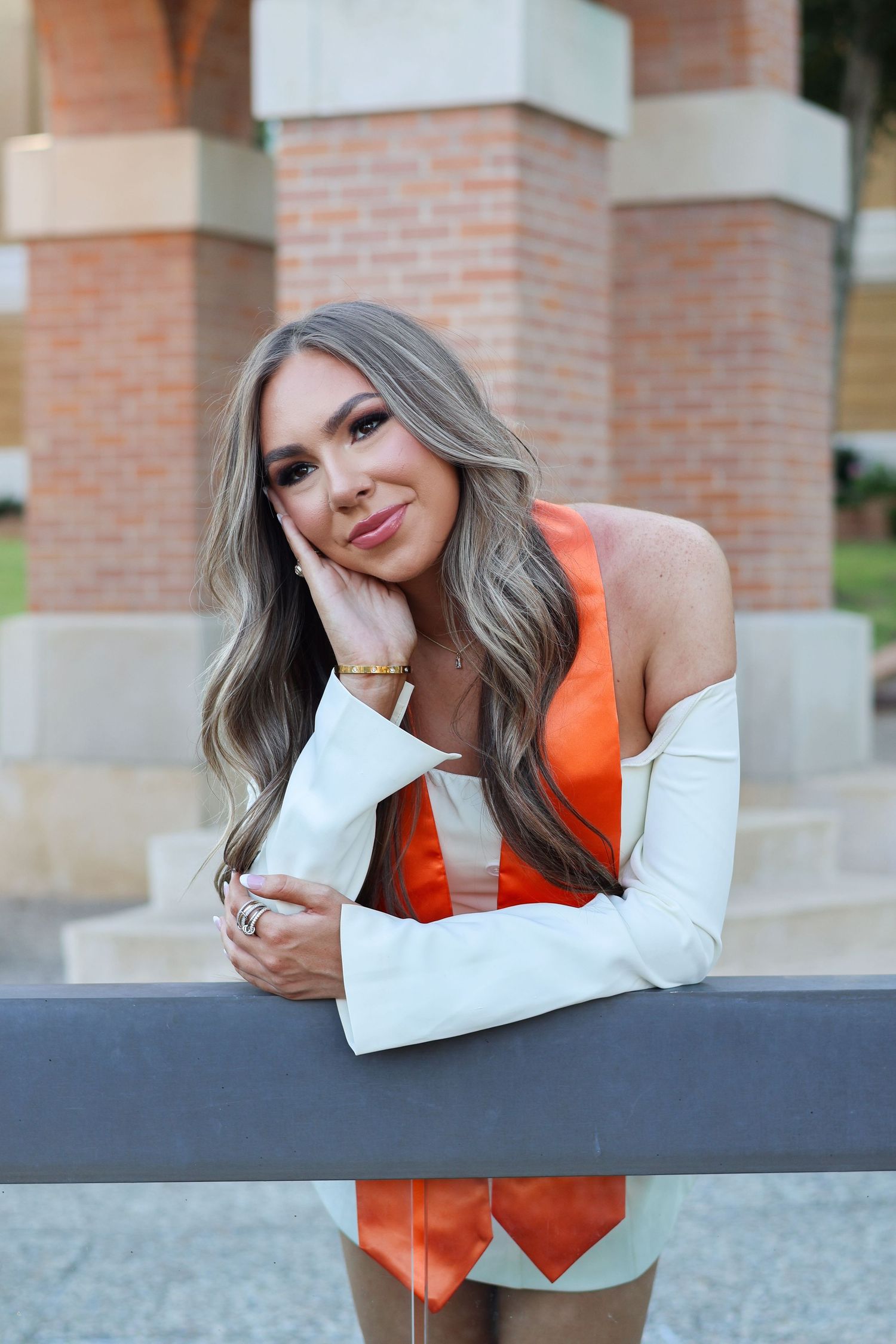 A person in an orange vest and white sleeves leans on a dark railing outdoors.