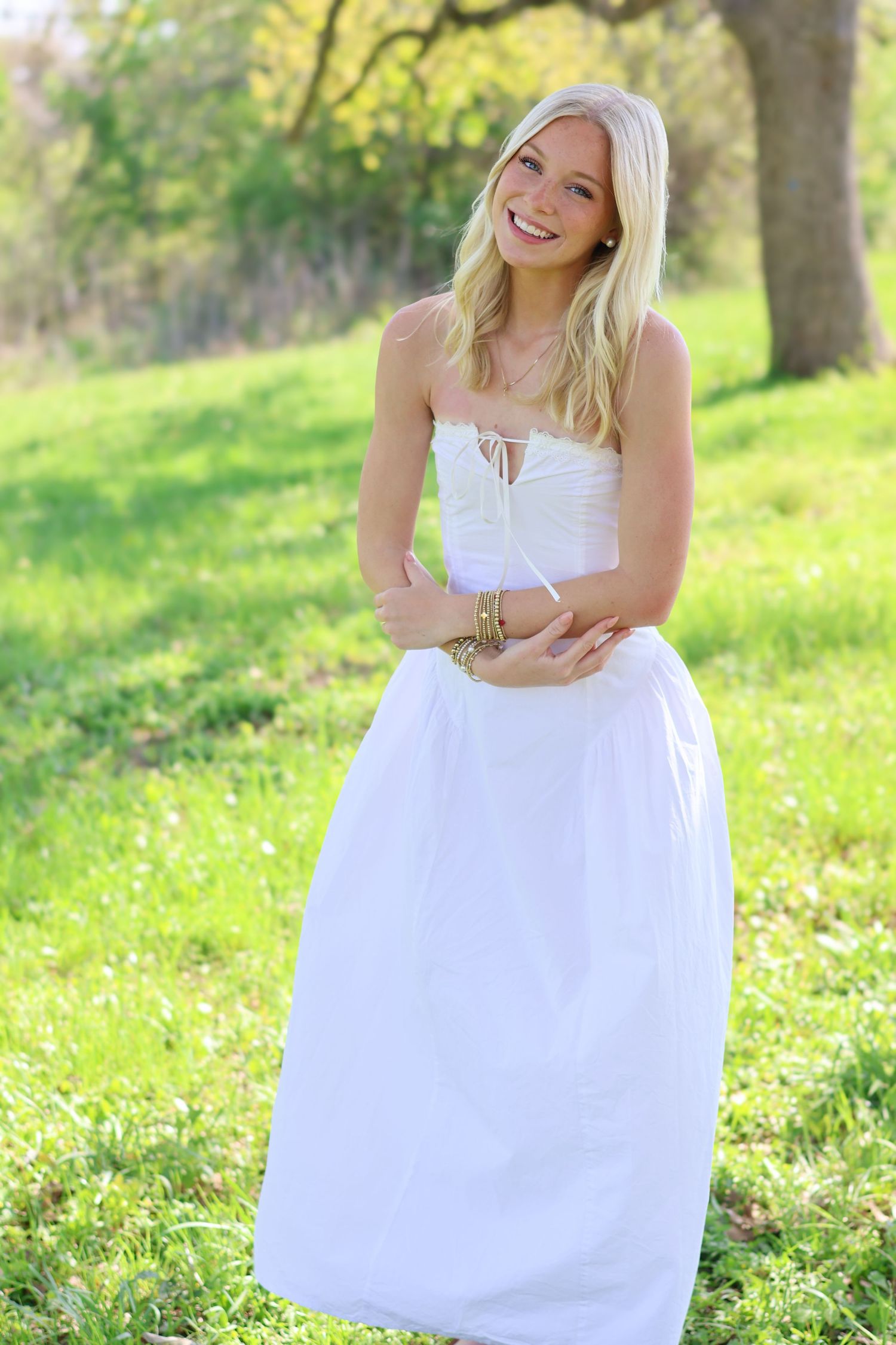 Smiling blonde woman in white sundress standing in green park.