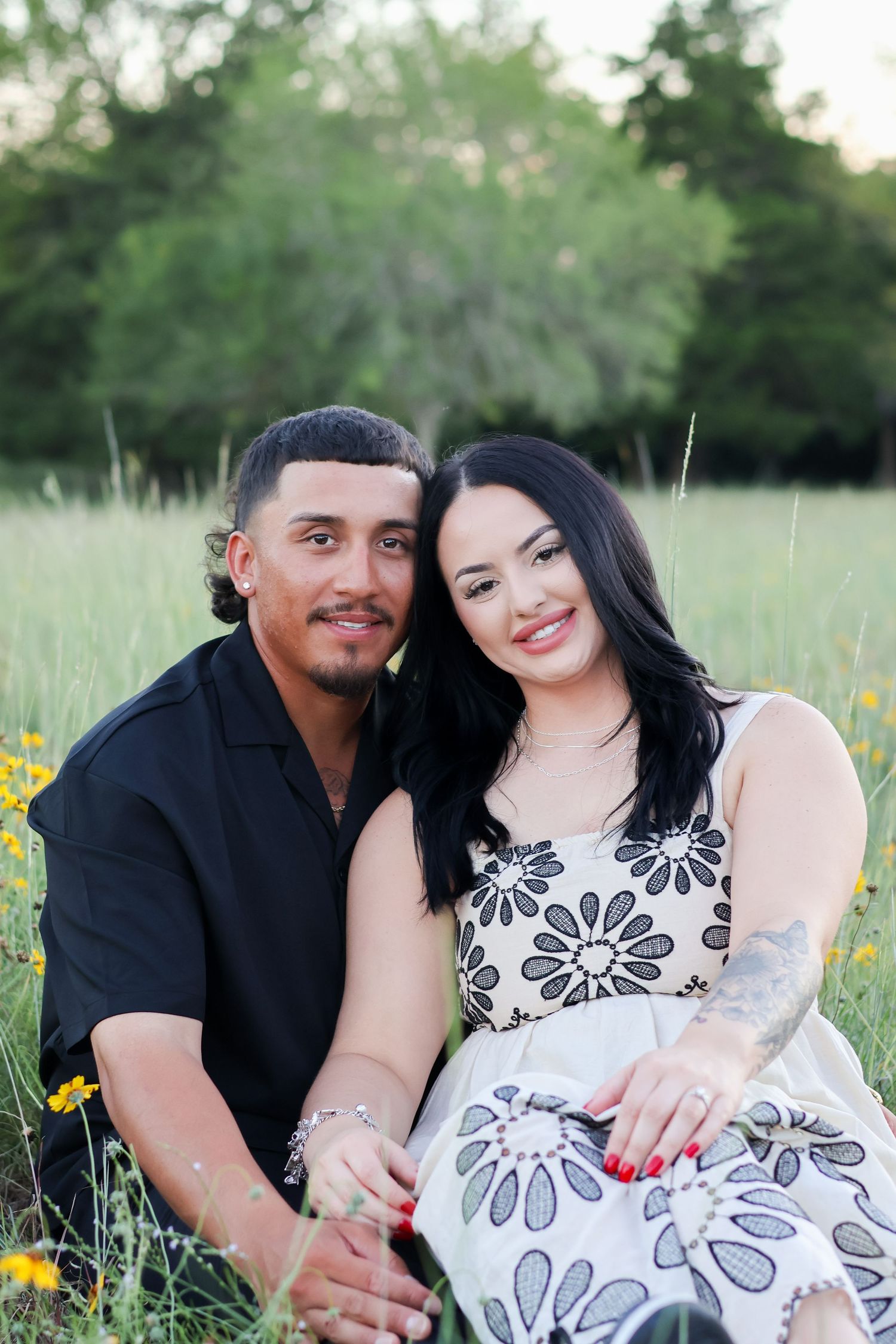 A couple sits together in a wildflower meadow at sunset wearing coordinated black and white outfits.