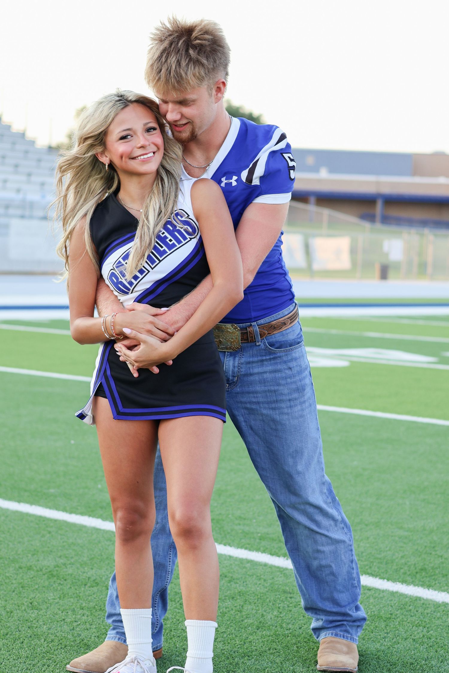 Couple in matching blue team attire embracing on football field.