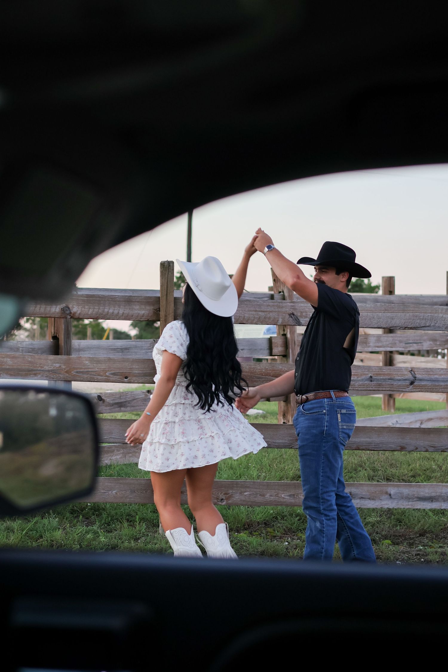 Playful wedding photography session near a rustic wooden fence in a countryside setting.