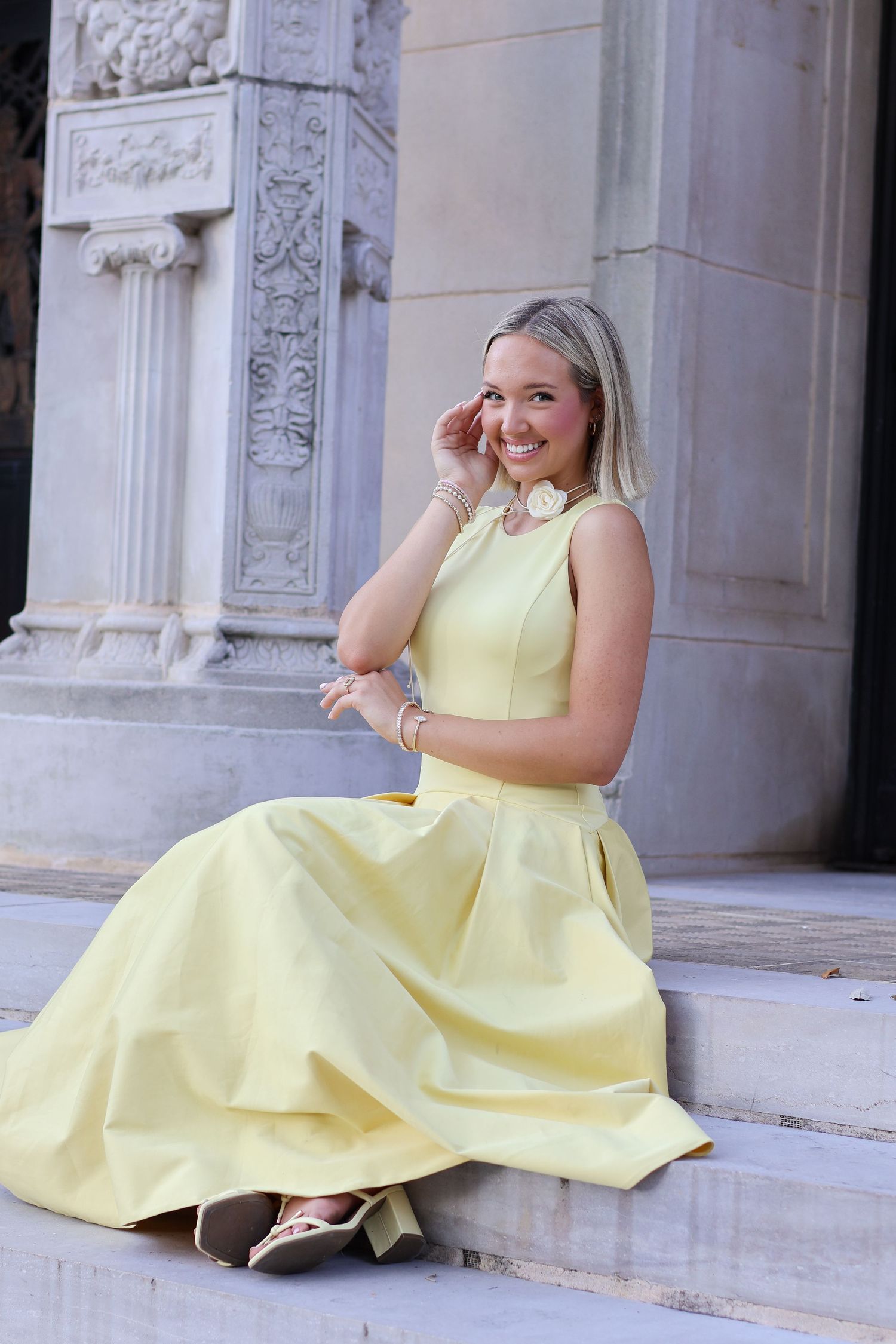 A person in a yellow sundress sits and poses on white stone steps in a series of connected photos.