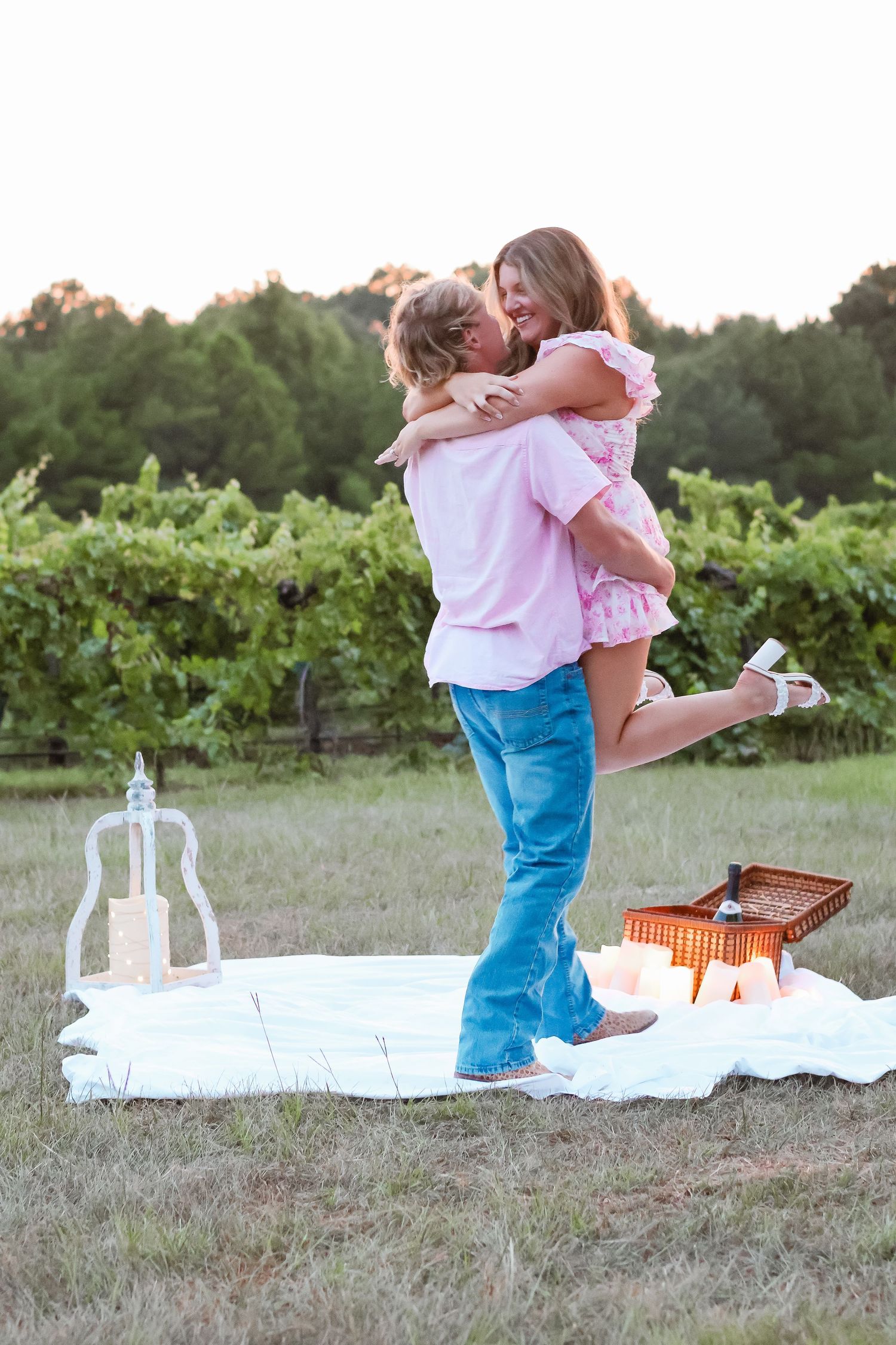 A child in blue jeans and pink shirt sits on a white blanket outdoors while opening a wooden box.