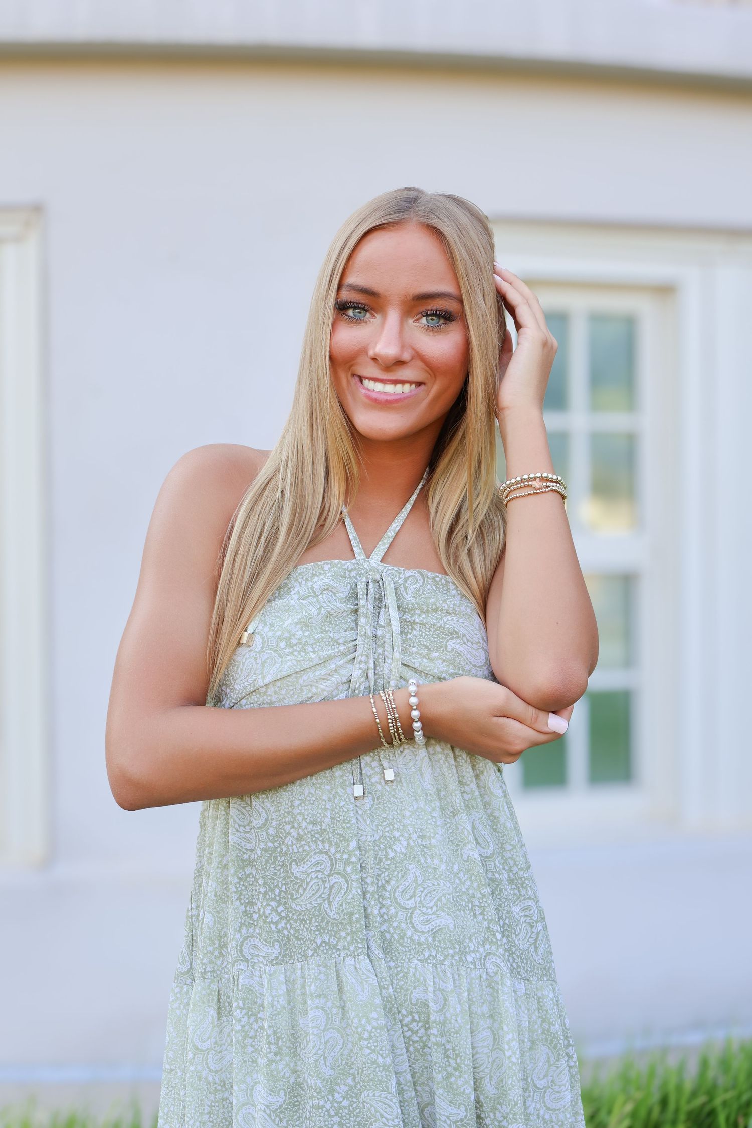 Woman in pale mint dress poses against white building exterior.