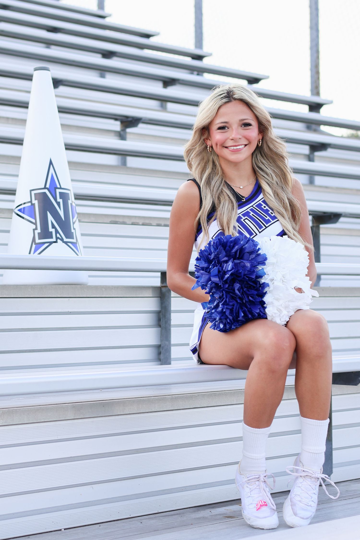 Cheerleader with pom poms poses on stadium bleachers.