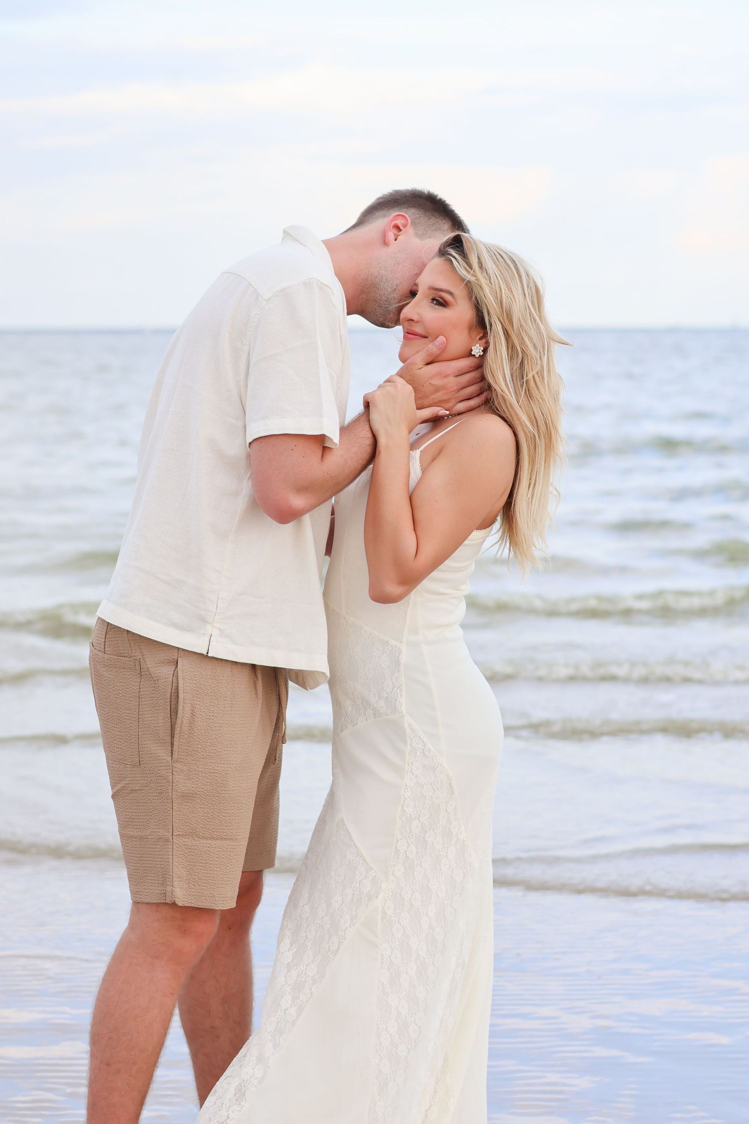 A romantic couple shares tender moments on a beach at sunset with waves in the background.