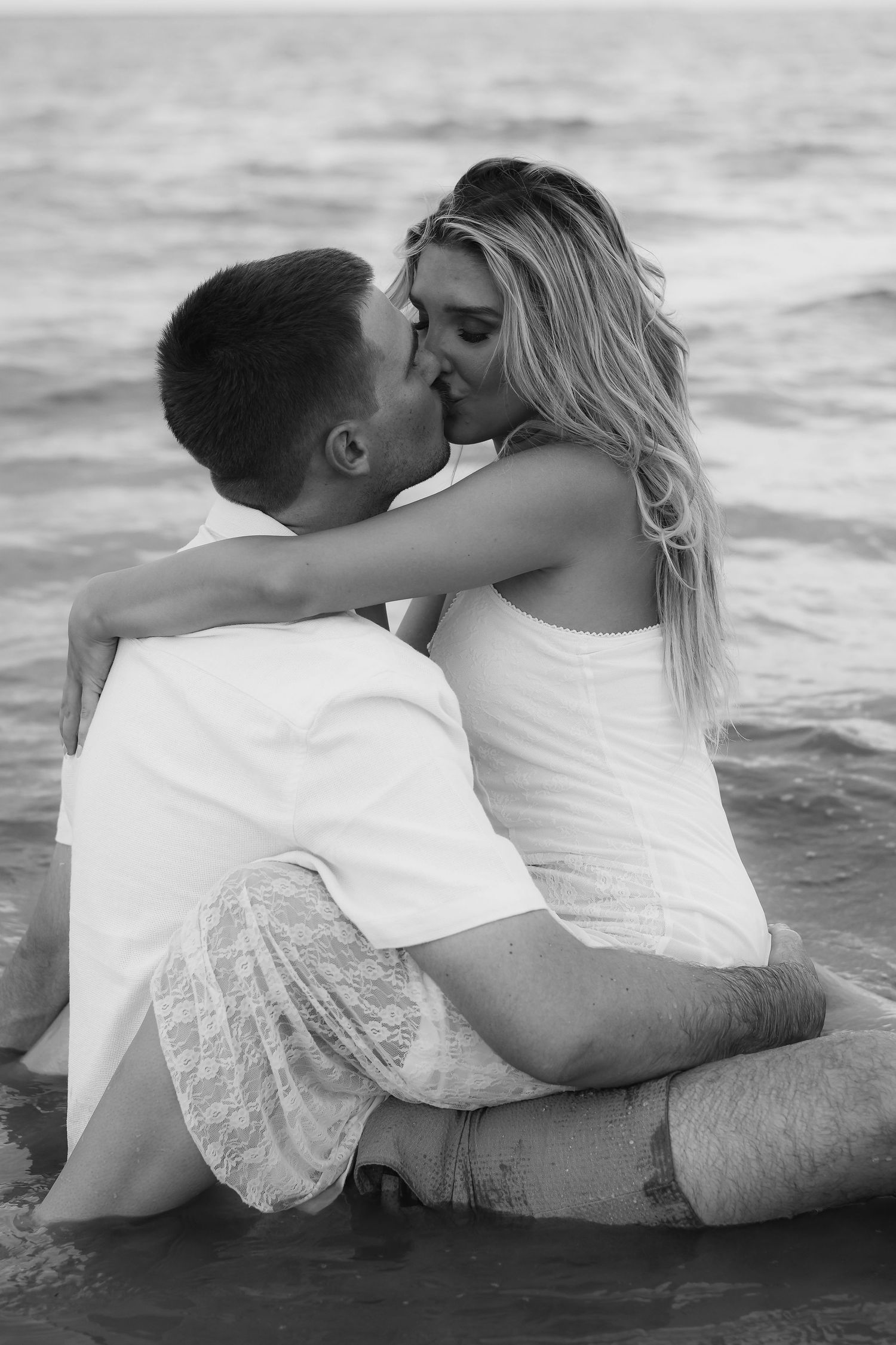 A romantic black and white photograph of a couple sharing an intimate moment while sitting at the beach.