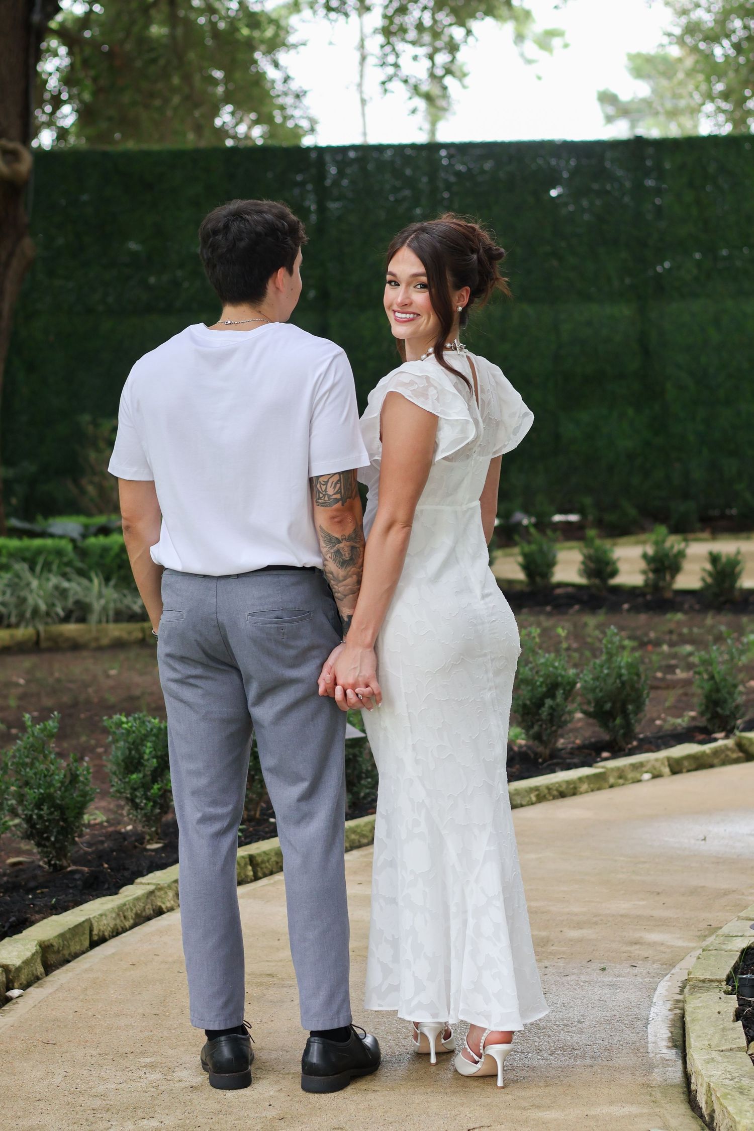 Three people walking together on a garden path in formal attire during an outdoor event.