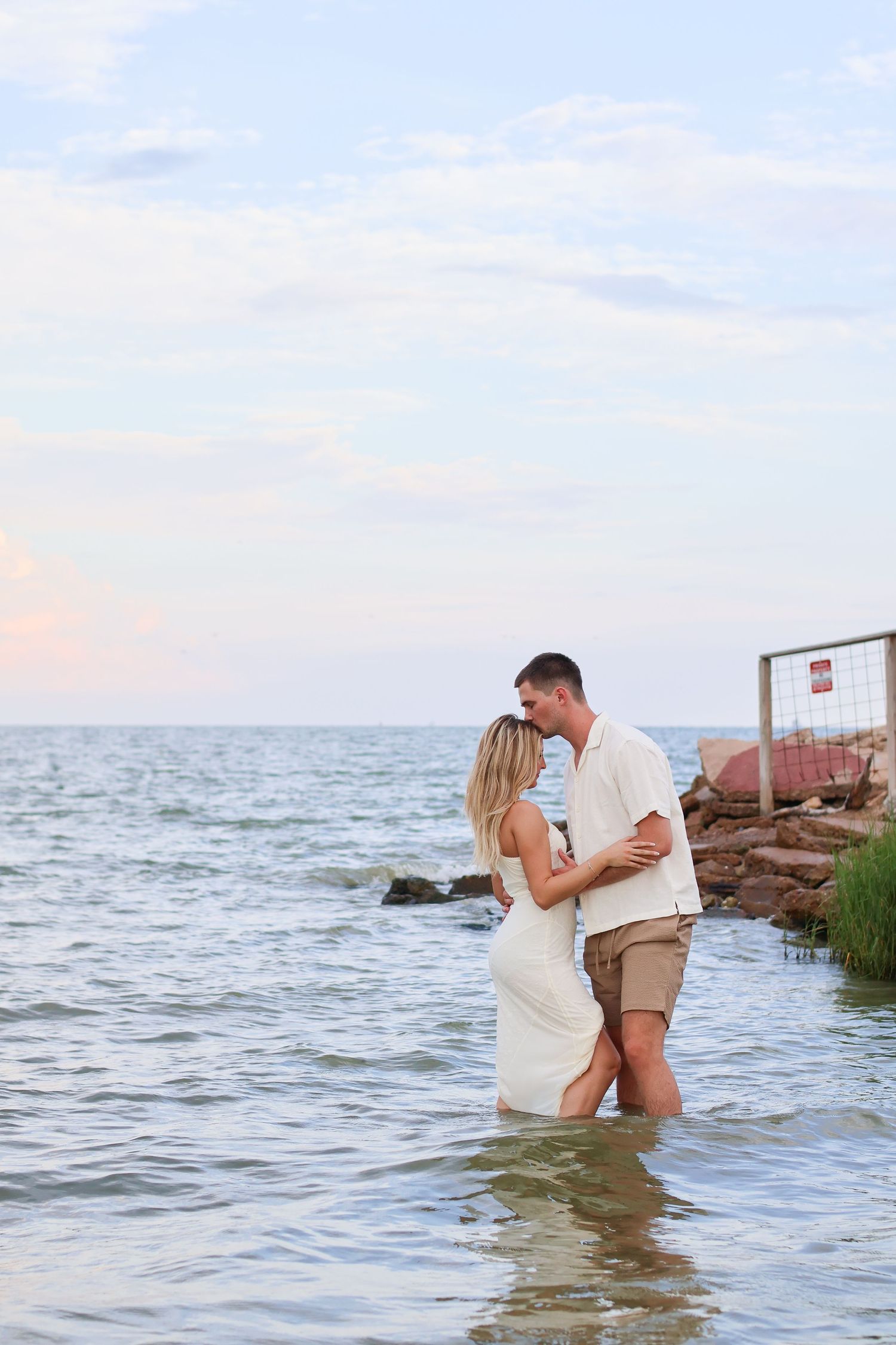 A couple in wedding attire shares romantic moments while standing in ocean water during a beach photo session.