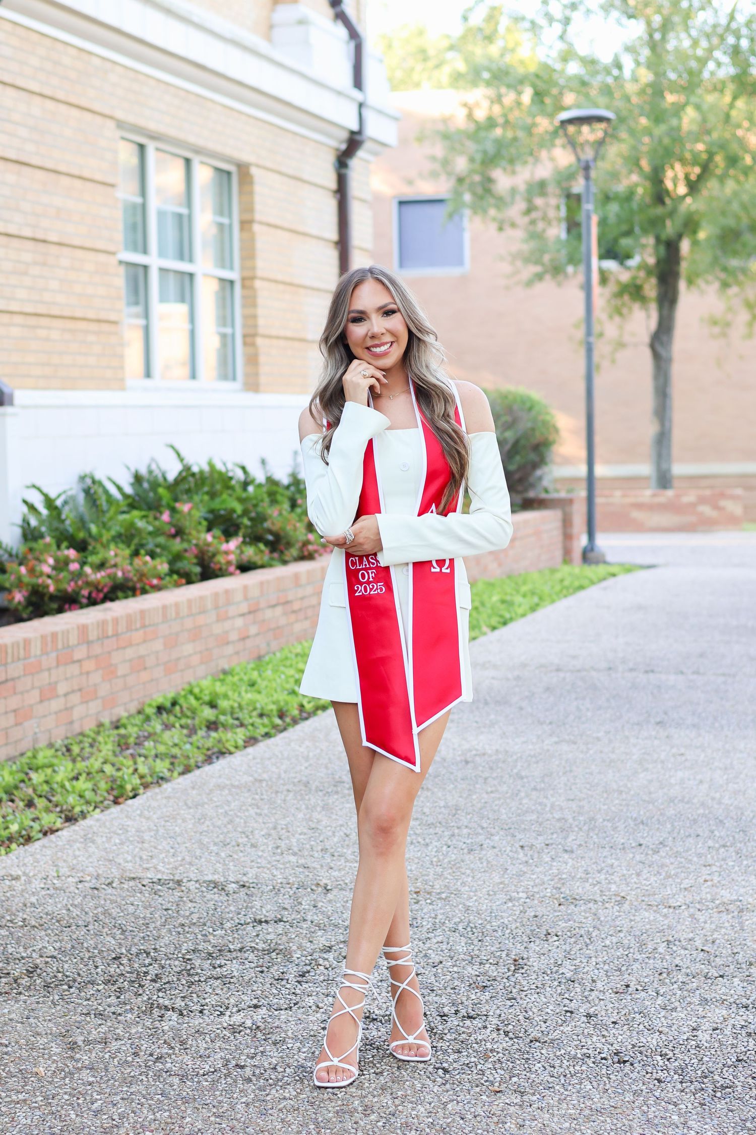 A stylish red and white dress outfit paired with strappy heels on a pathway near a brick building.