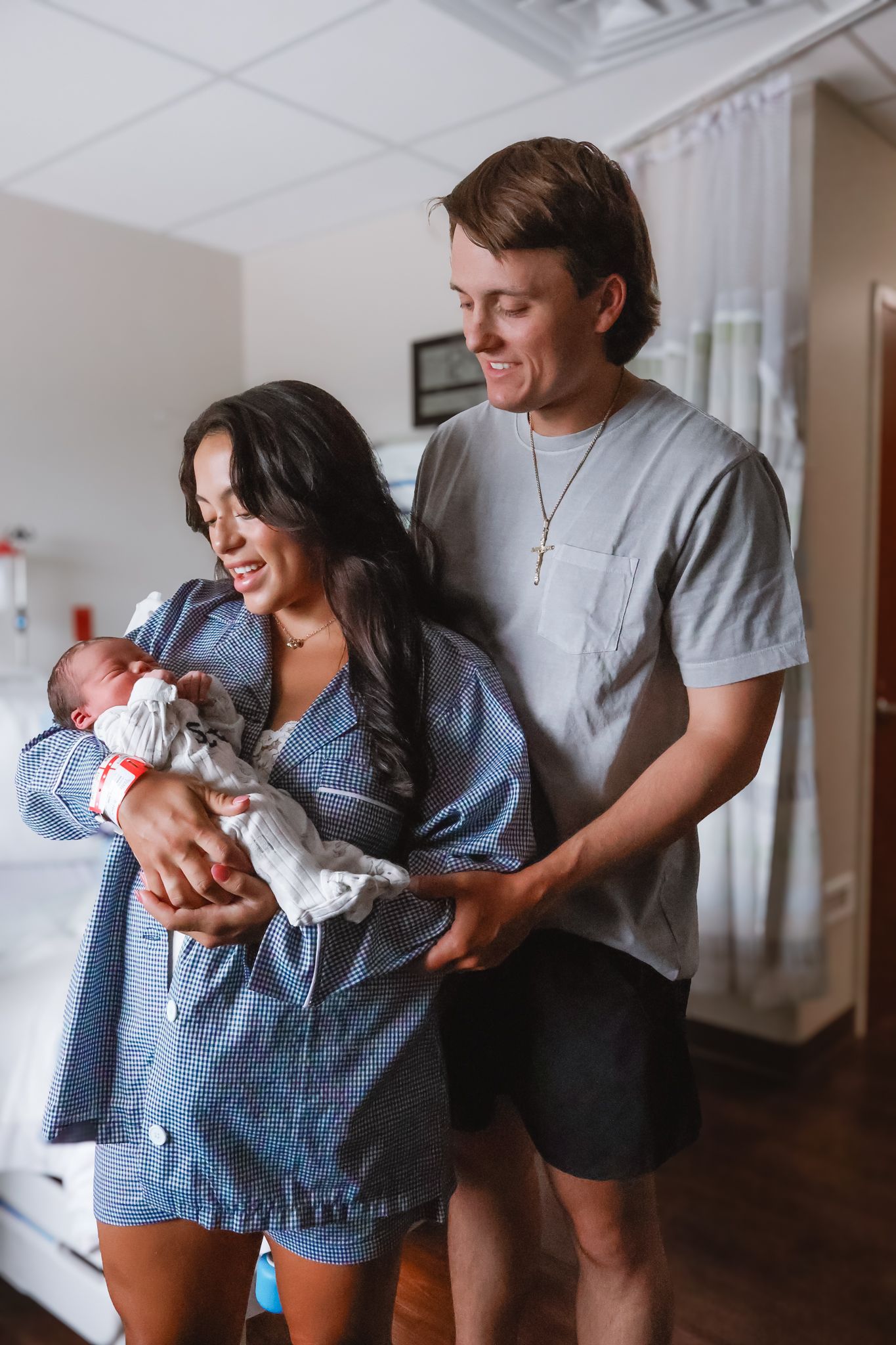 New parents share a tender moment with their newborn baby in hospital room.