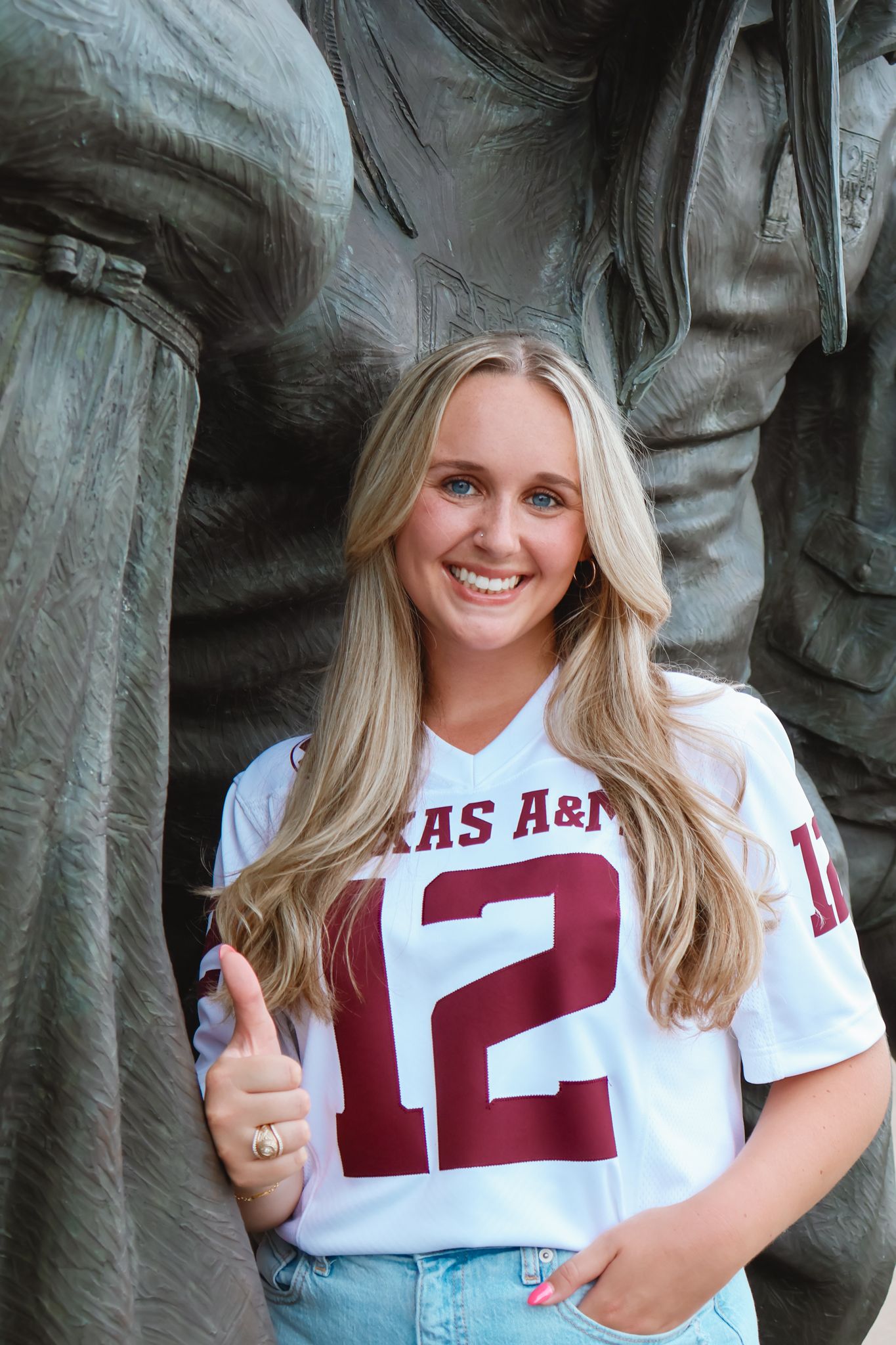 Student in Texas A&M jersey number 12 poses confidently by campus statue.
