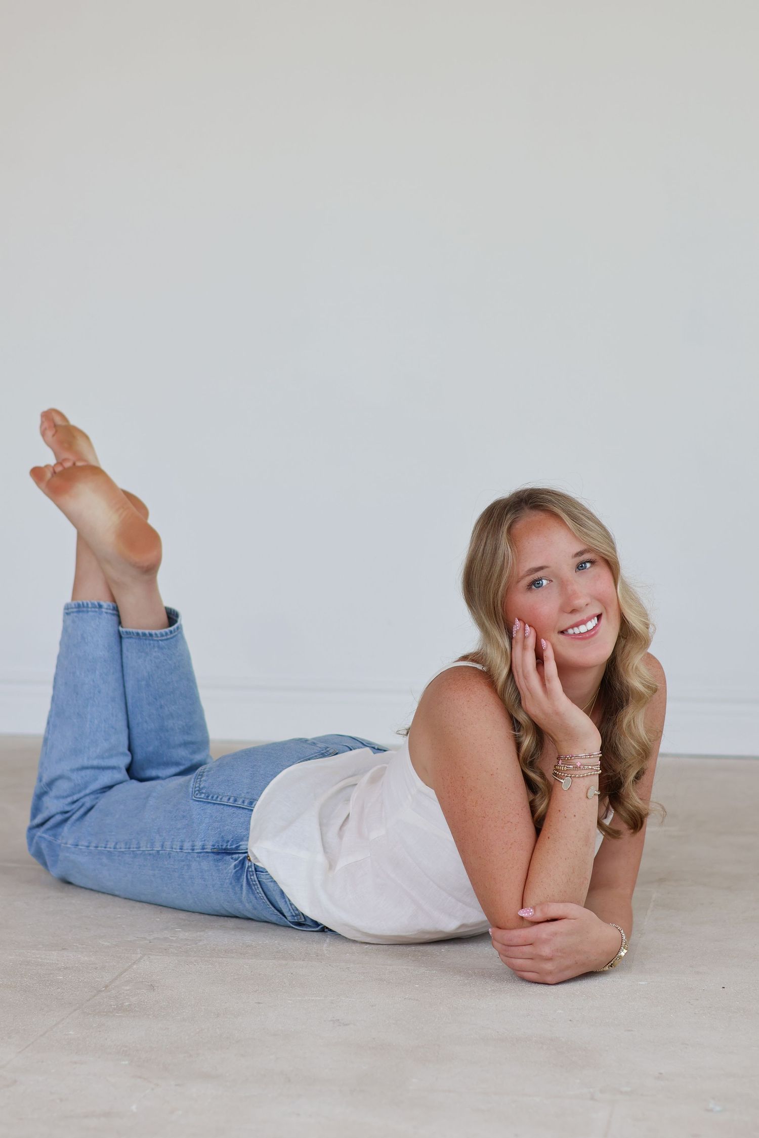 Person in white top and blue jeans lying on floor in casual poses against light background.