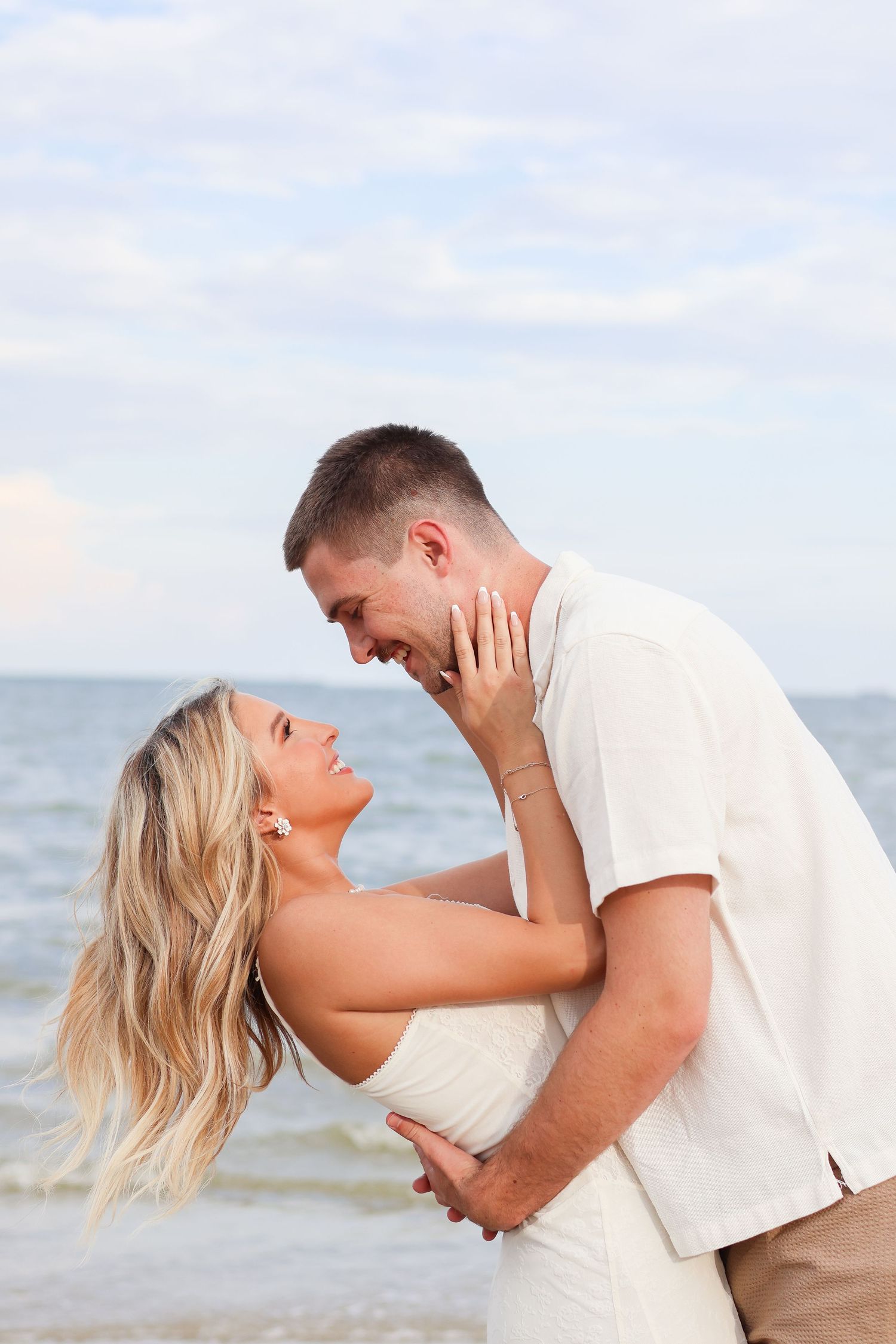A romantic couple embraces and laughs together during a beach photoshoot at sunset.