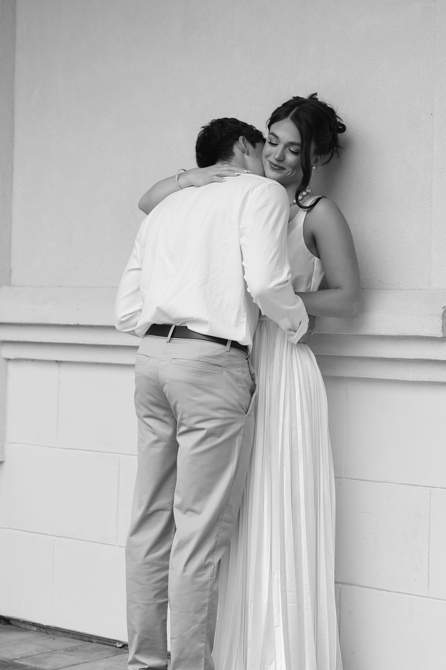 Black and white photo sequence showing a couple in white dress and khaki pants embracing against a wall.