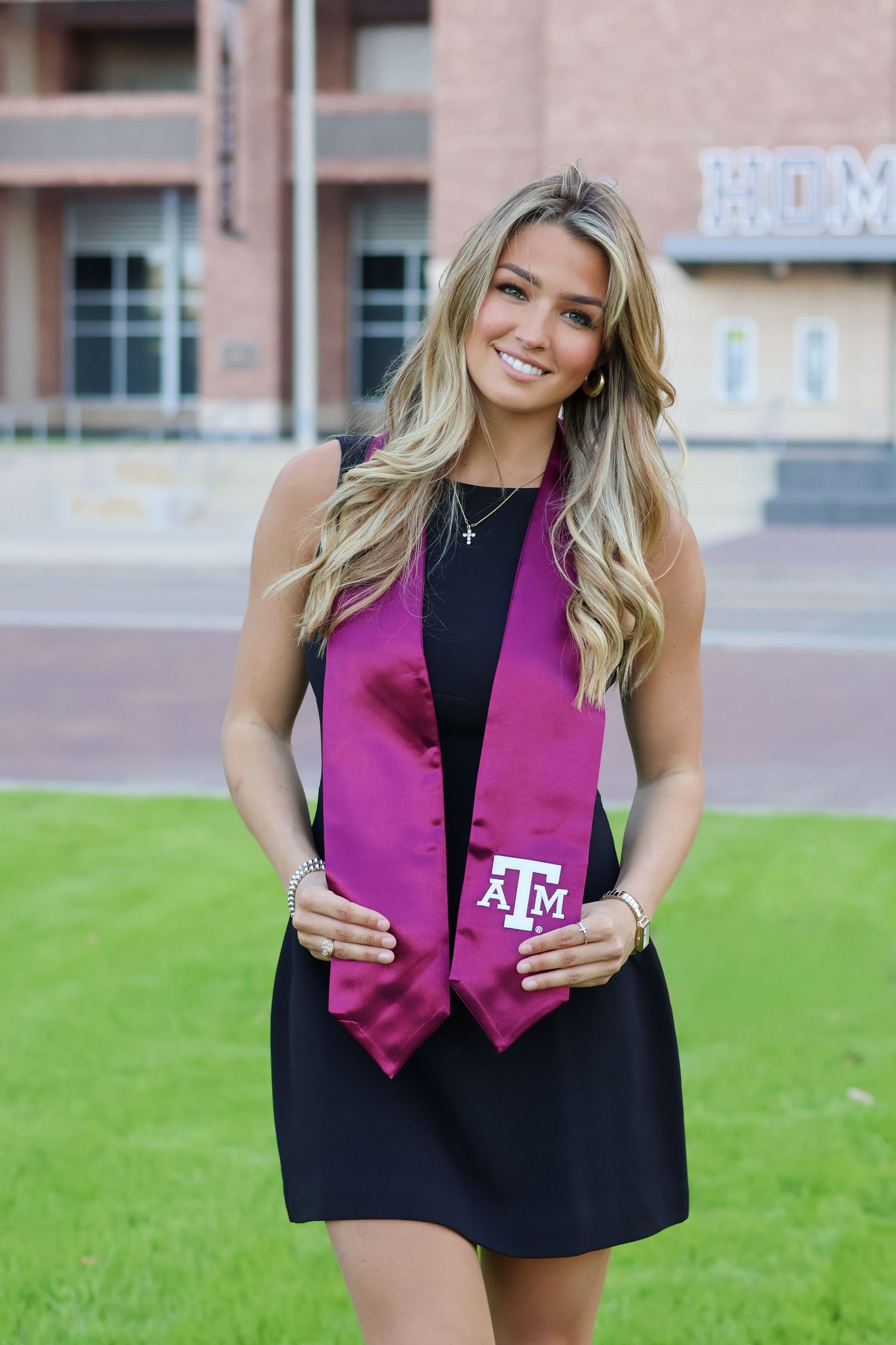 Smiling woman in black dress with Texas A&M maroon graduation stole.