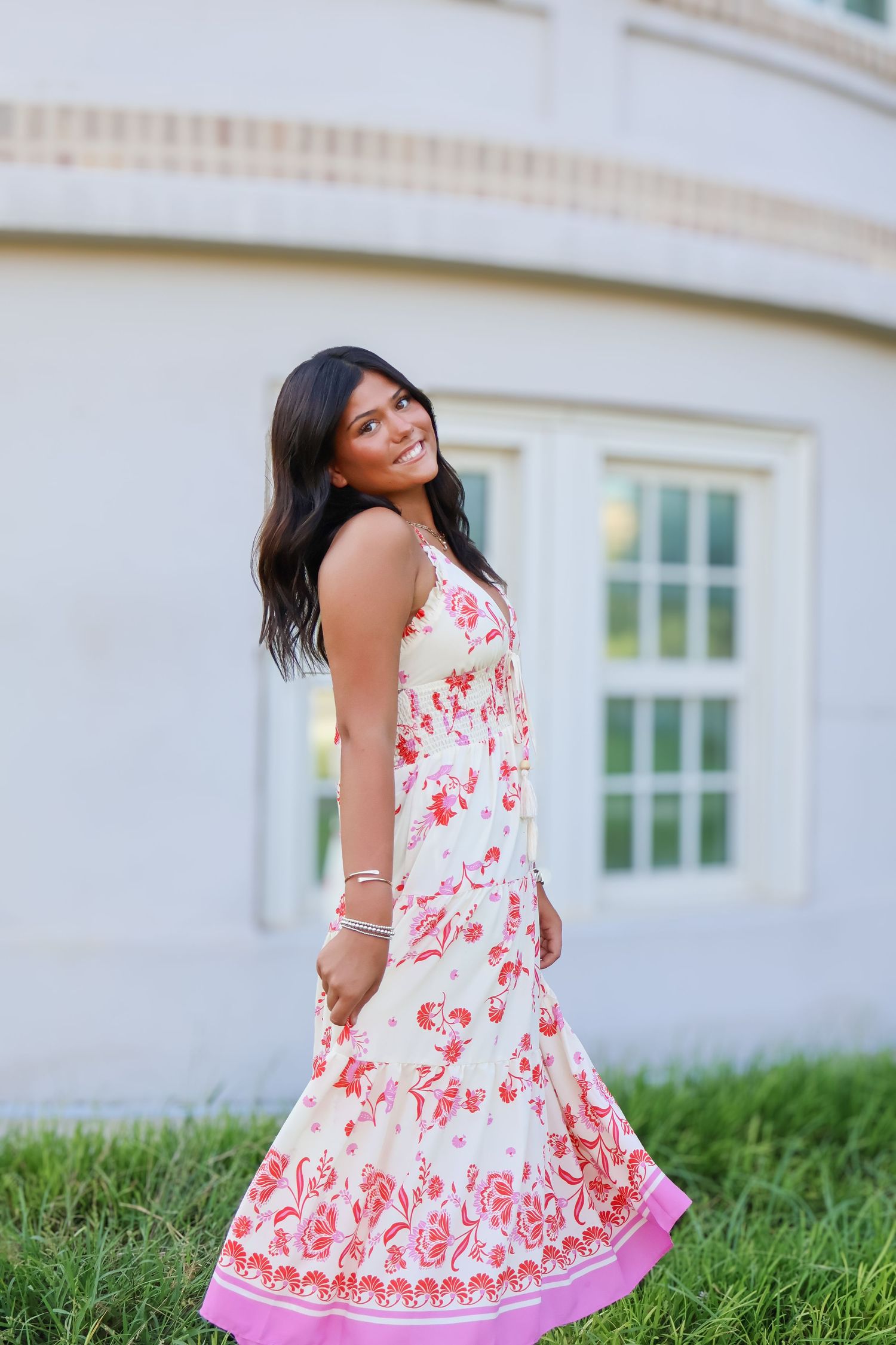 Woman in floral print dress twirling outside white building.