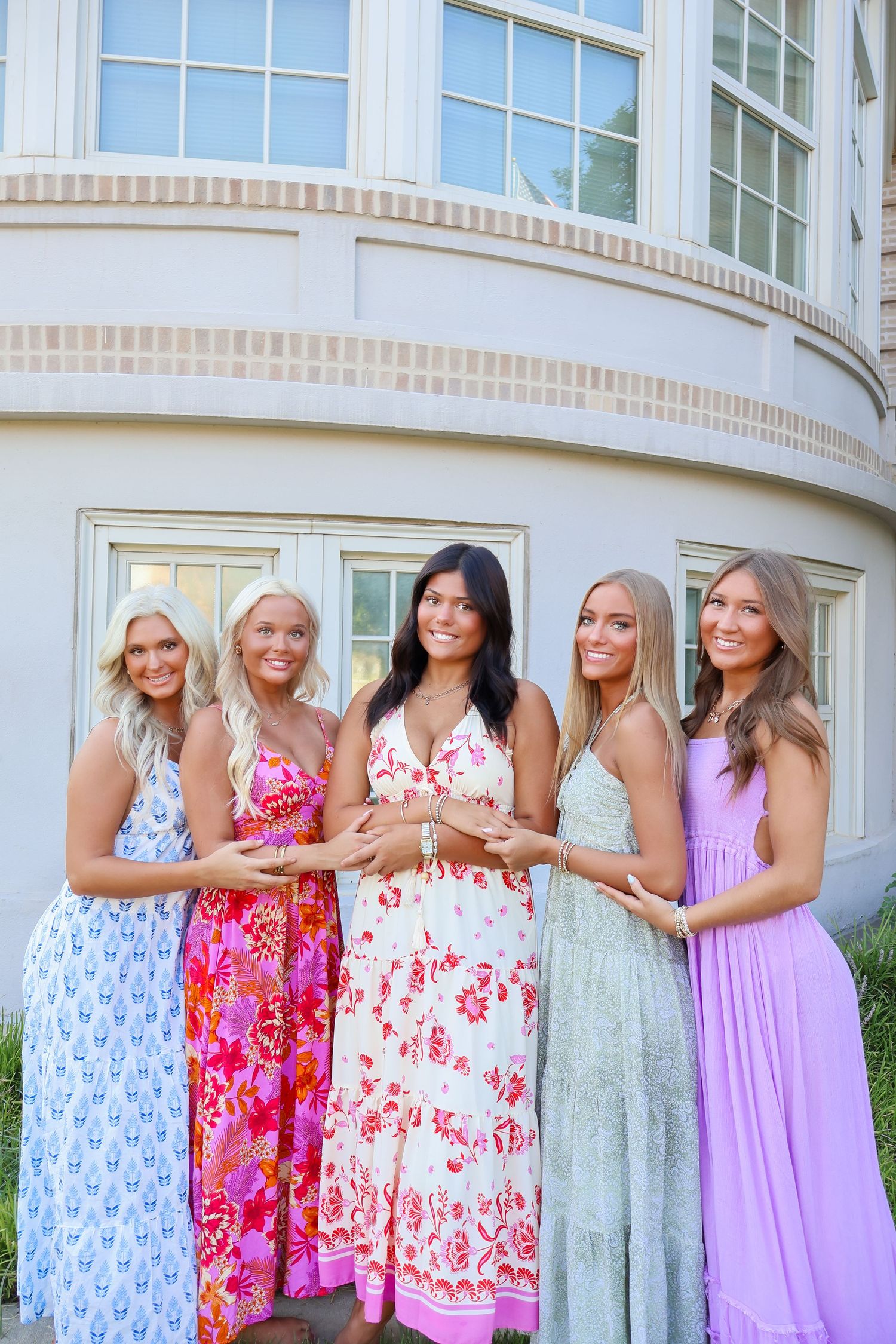 Group of women in colorful floral and pastel dresses posing together outside a building.