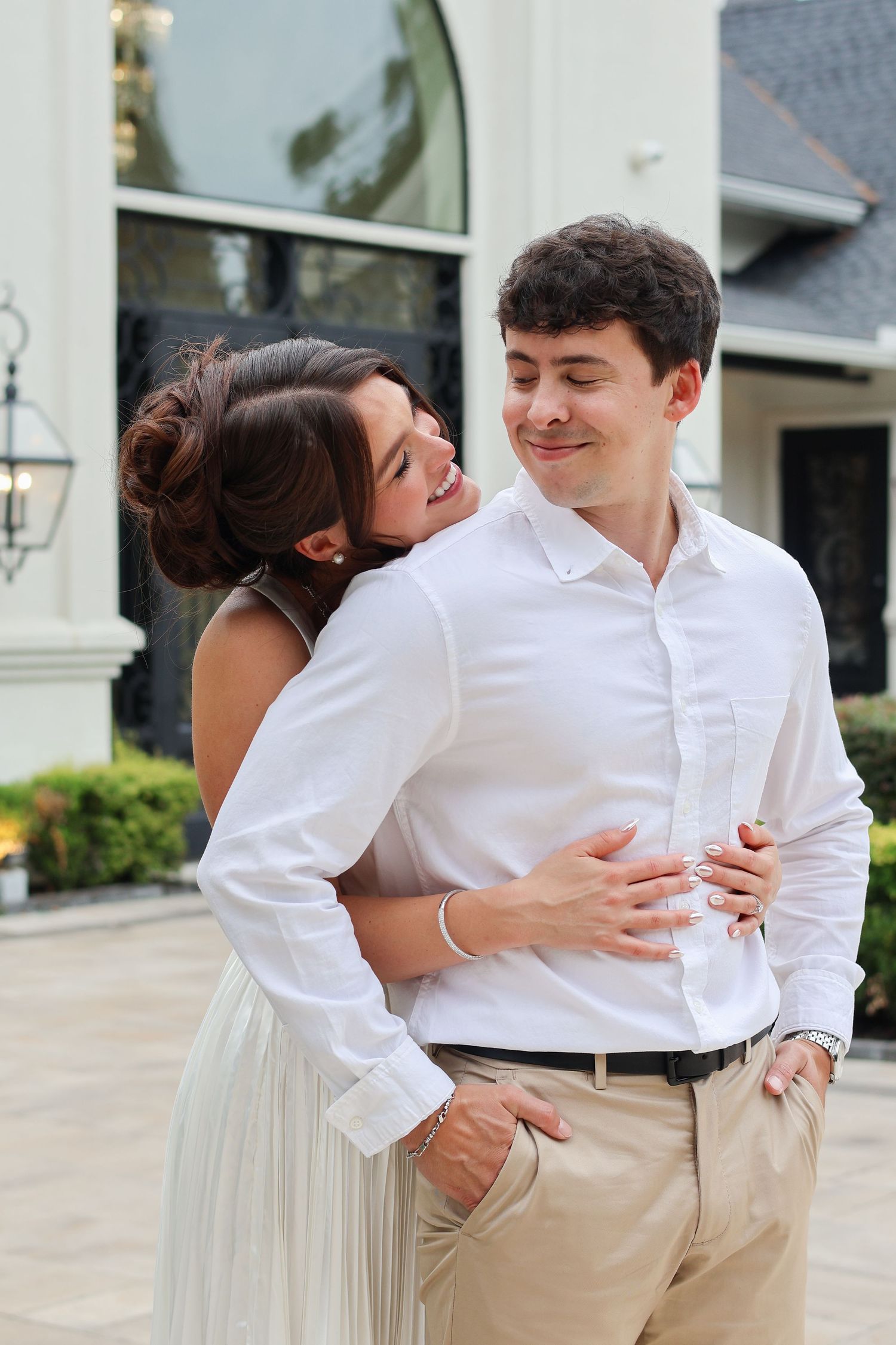 A couple in white and khaki outfits embrace and smile lovingly during an outdoor photoshoot.
