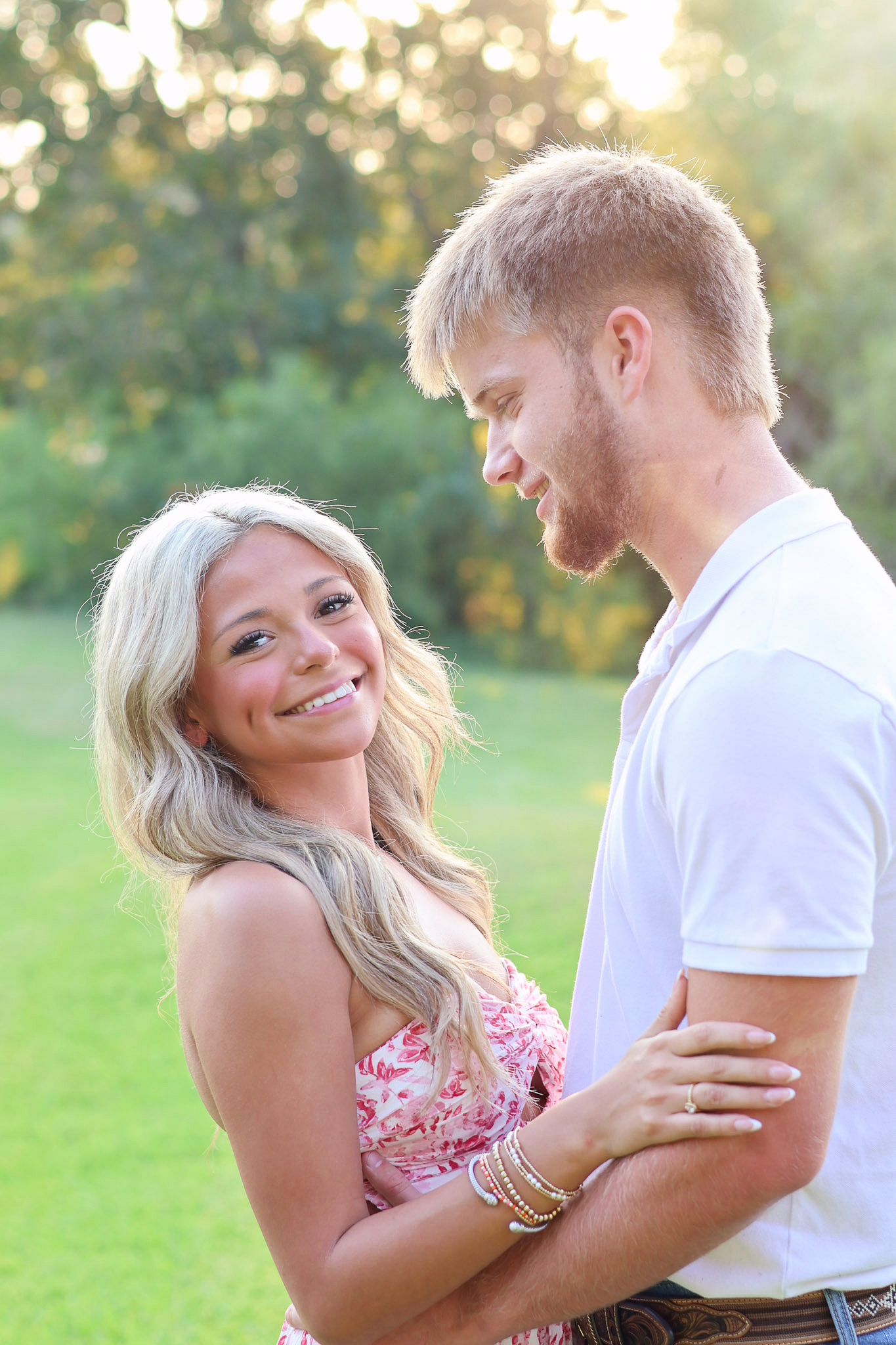 A couple shares tender moments in a sunny outdoor setting with the woman wearing a pink floral dress.