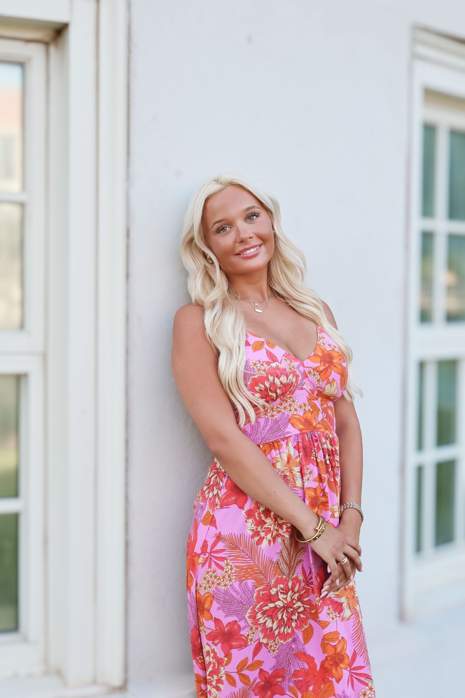 A bright pink and orange floral print sundress shown in multiple poses against a light wall.