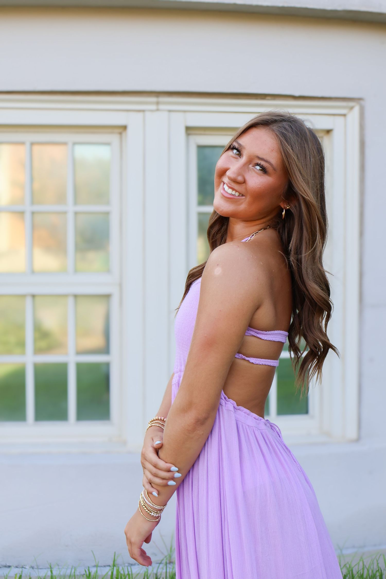 Young woman in pink dress poses gracefully against white building background.