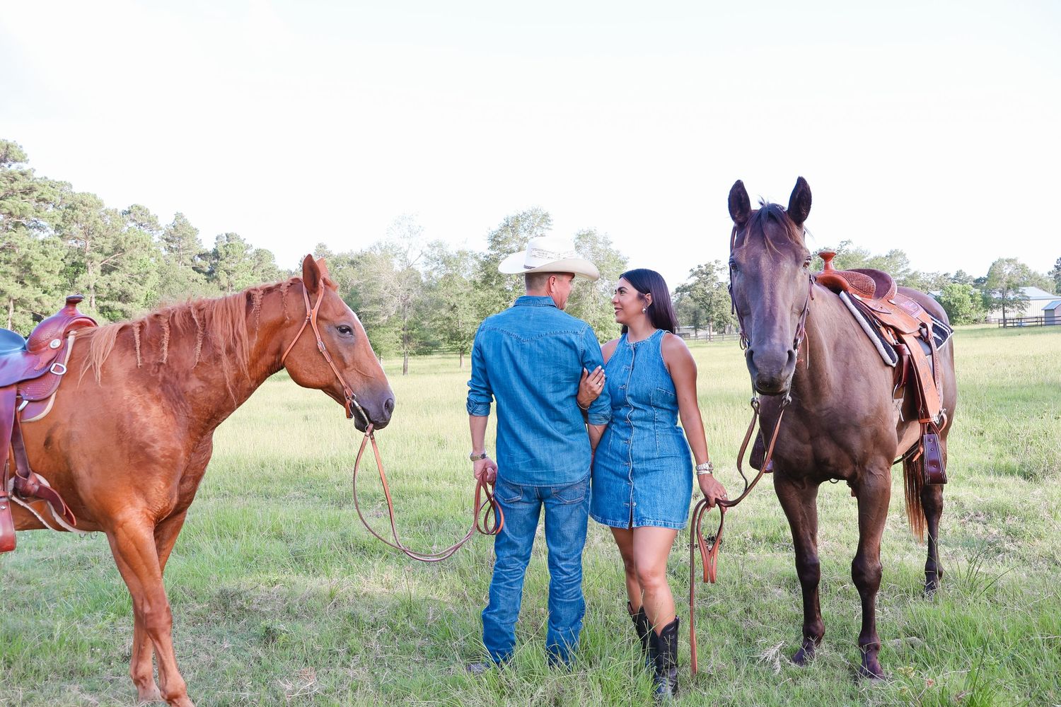 Couple poses with horses in a rustic field wearing matching denim outfits.