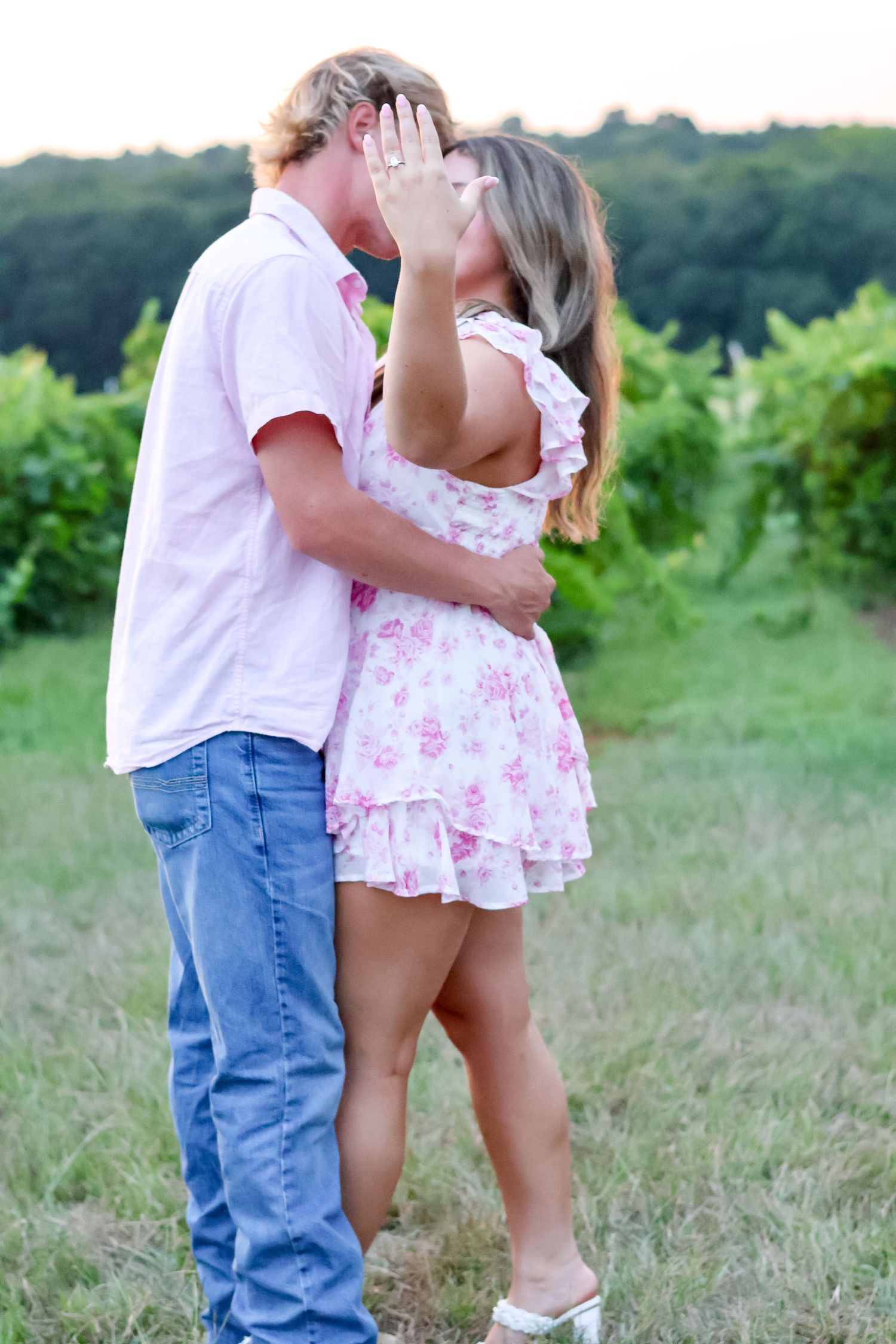 A couple embraces in a romantic moment while standing in a grassy summer field.