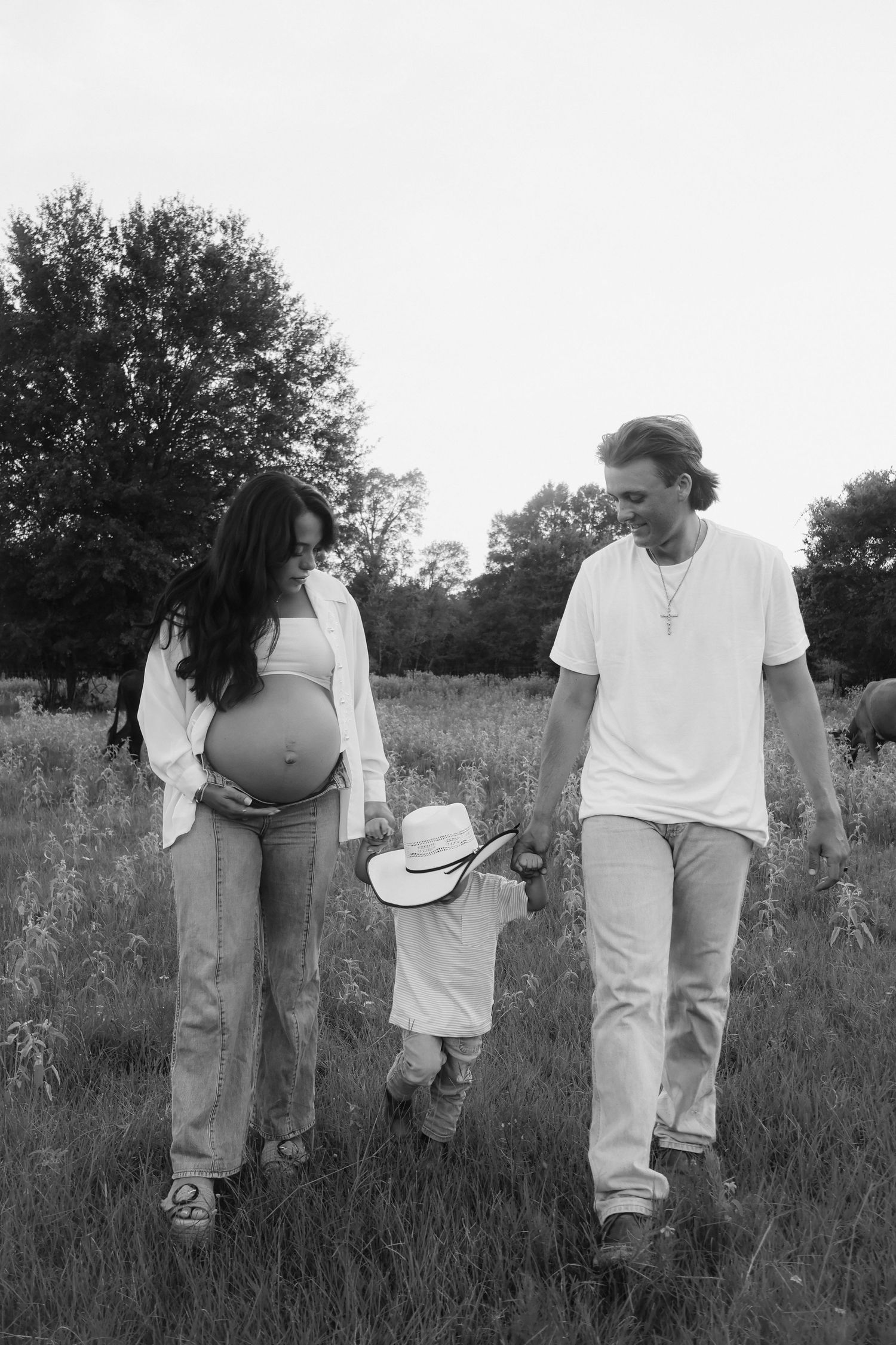 Black and white photograph of family walking through tall grass field together.