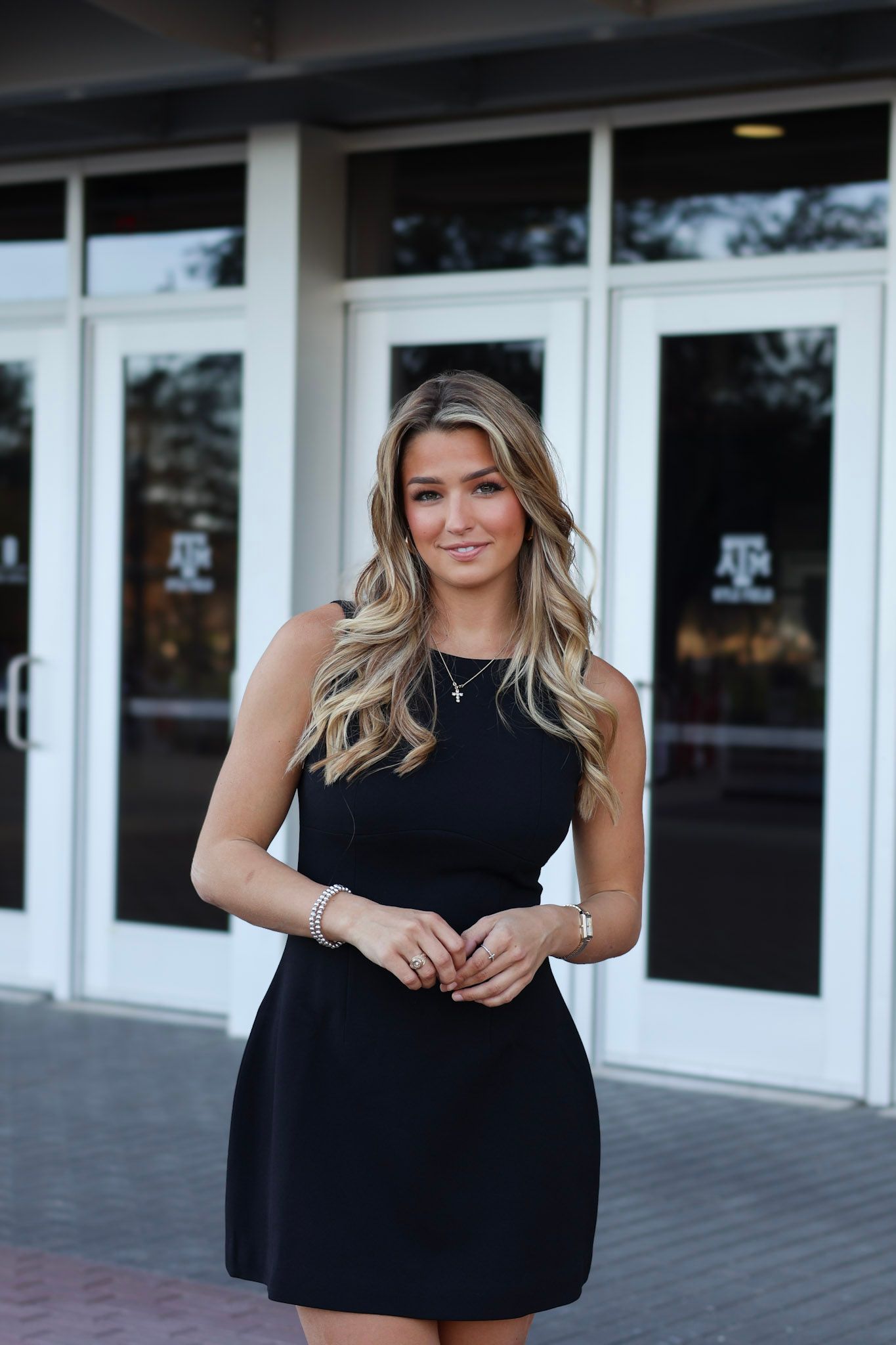 Young woman in black sleeveless dress with blonde hair posing outside Texas A&M athletics building.
