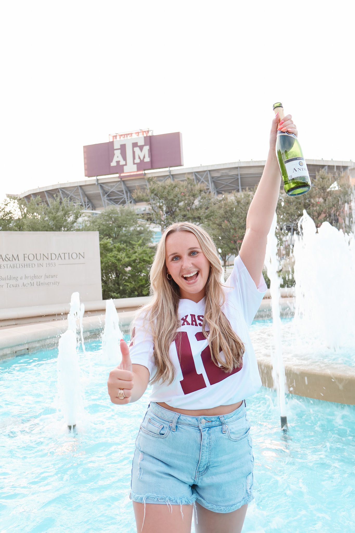College students celebrating by a fountain wearing Texas A&M gear and denim shorts.