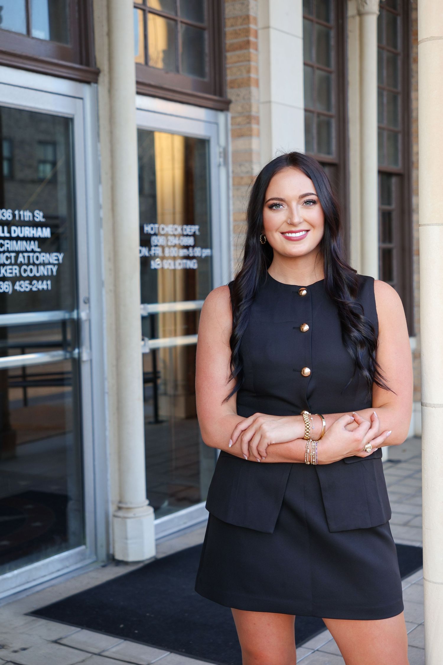 Professional woman in a black sleeveless top and brown shorts poses confidently outside an office building.