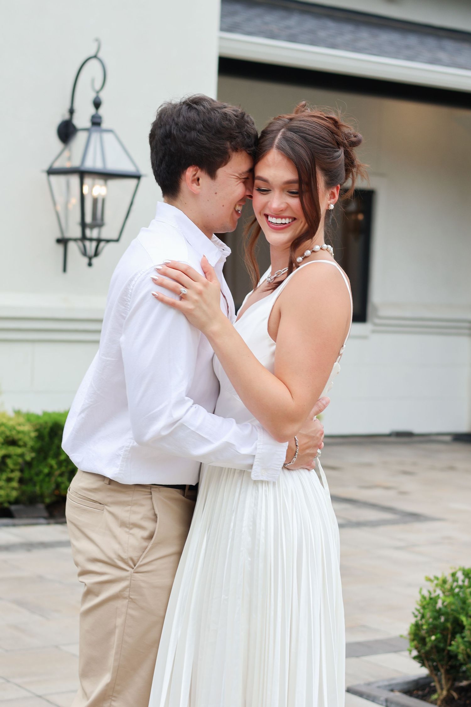 A couple shares a tender embrace on a patio wearing white and khaki outfits in a series of romantic photos.