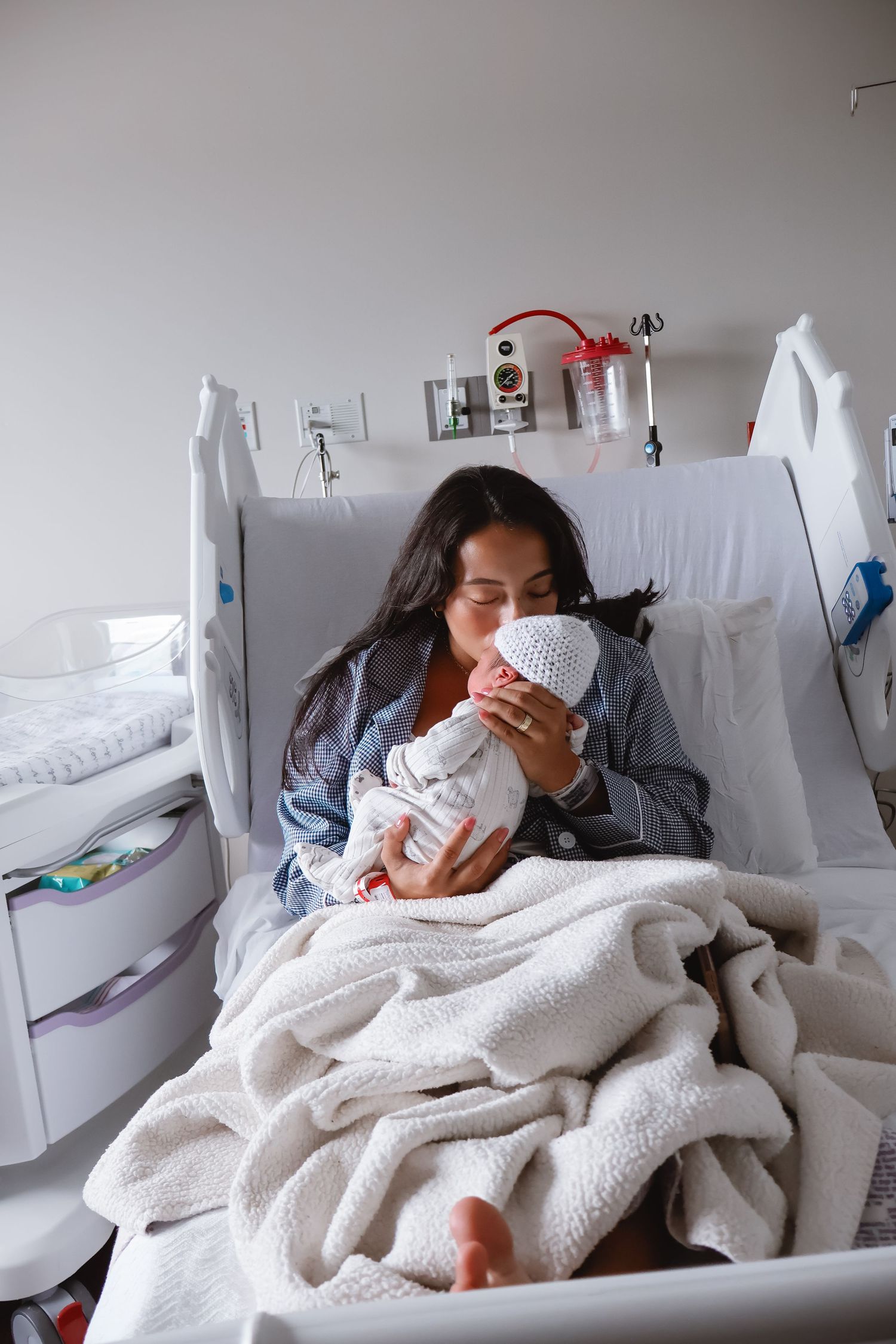 Mother and newborn resting together in hospital bed covered with soft white blanket.