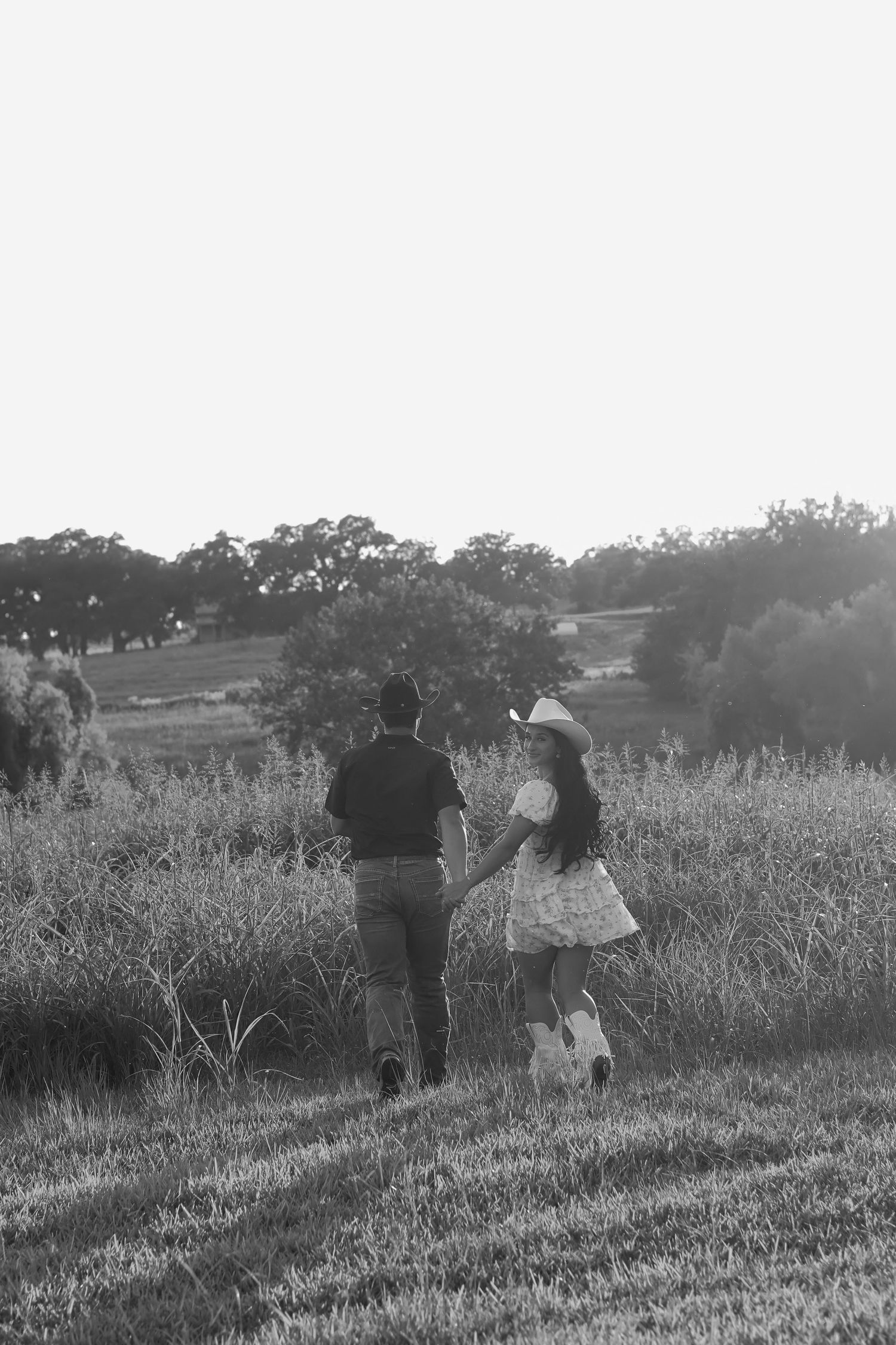 A couple walks together through a scenic meadow at sunset in black and white photography.