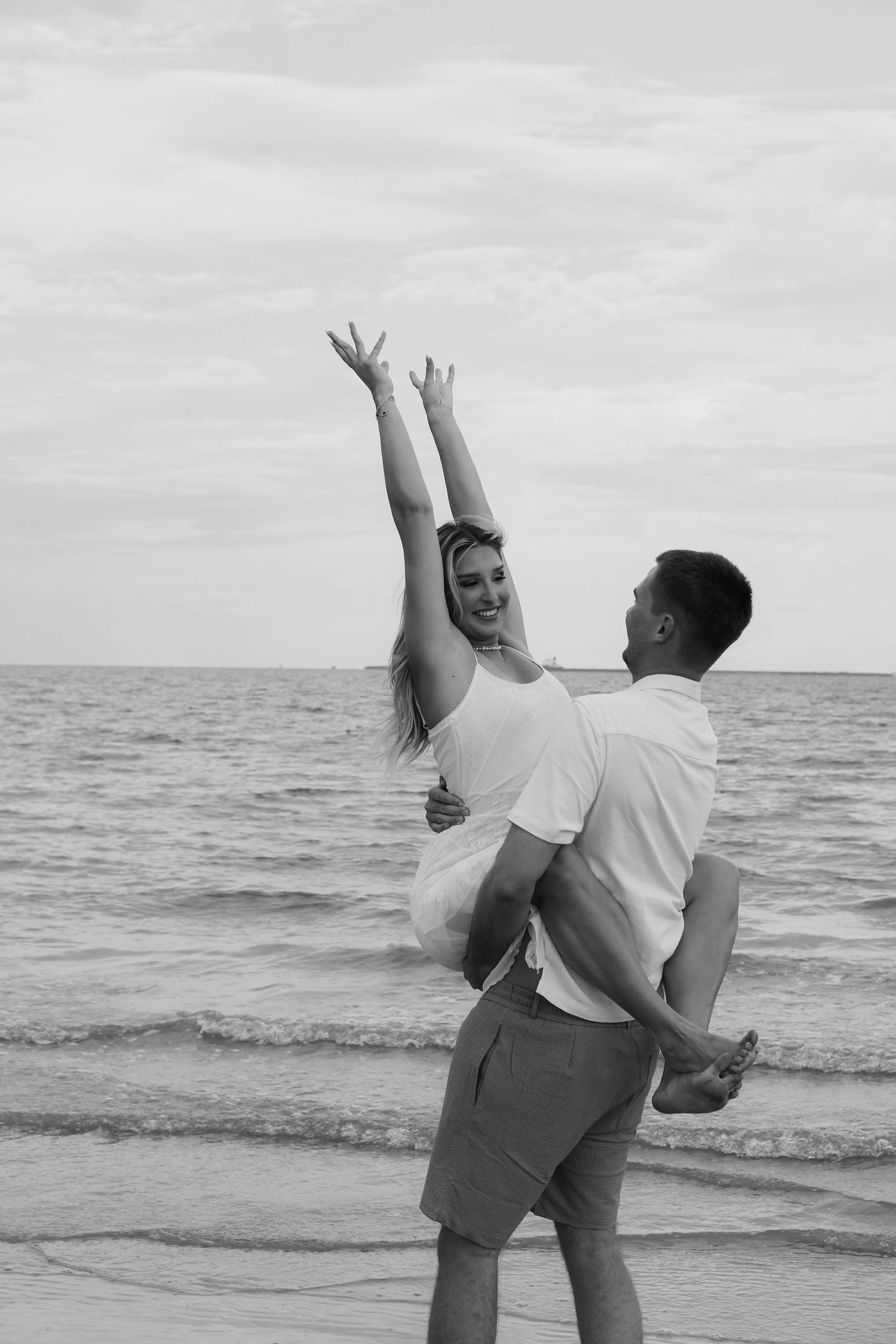 A playful couple enjoys a romantic moment at the beach shore in black and white photography.